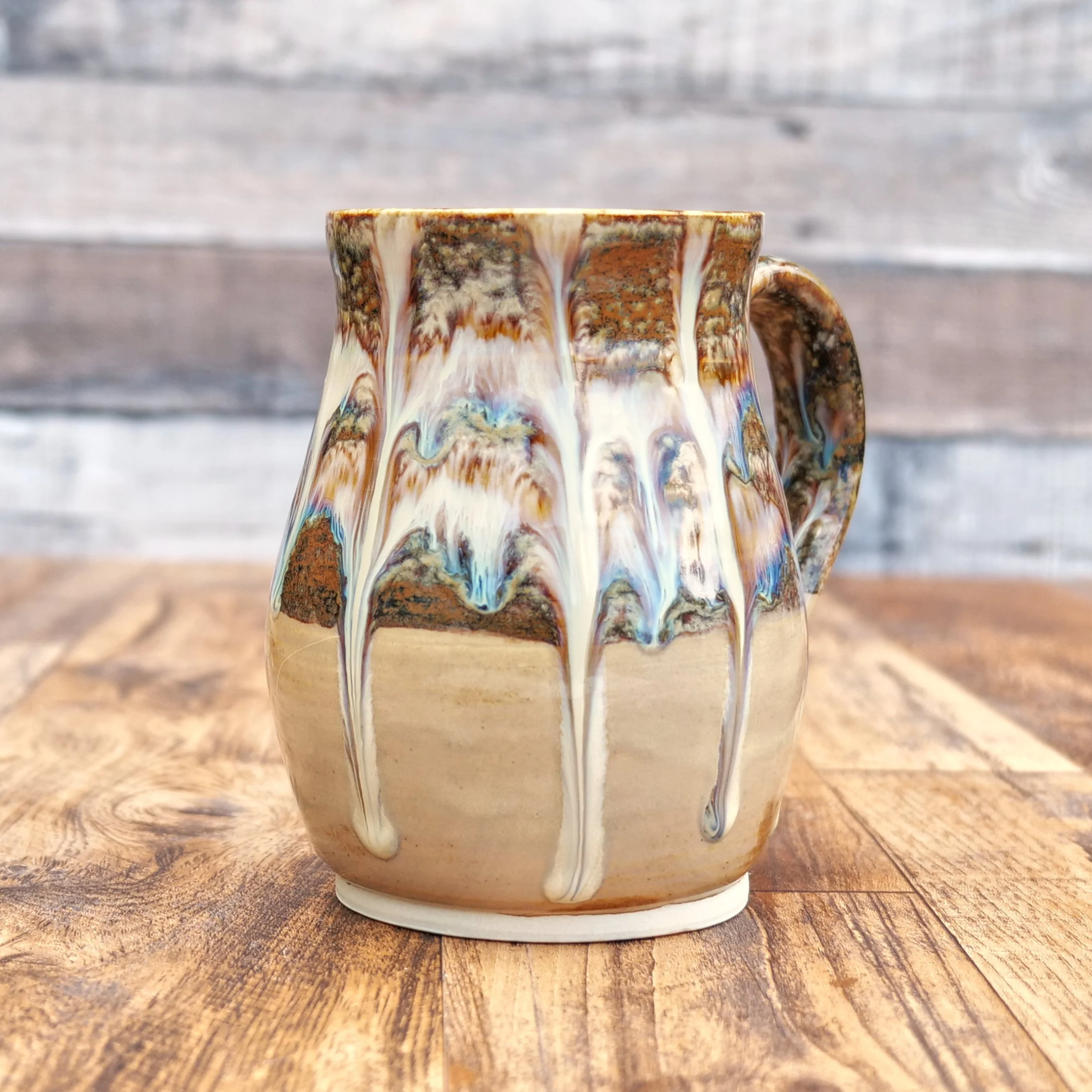 Handmade stoneware Cascade Mug by Elderkiln Ceramics featuring flowing layered glazes in earthy brown, cream, and mineral tones on a rustic pottery mug.