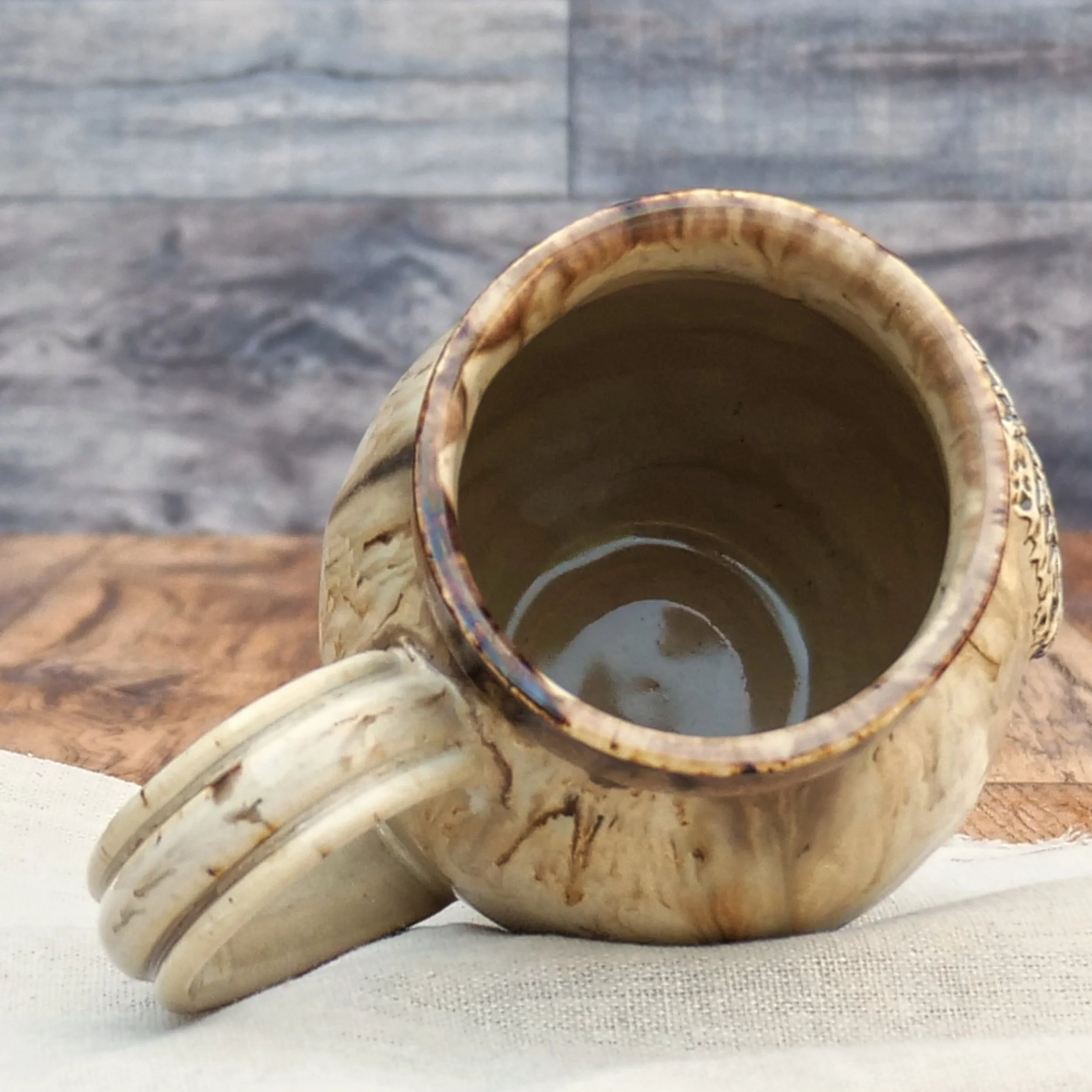 Handmade Wayfinder Mug by Elderkiln Ceramics featuring a sculpted Vegvísir symbol and layered earthy stoneware glazes in cream, amber, and brown tones.