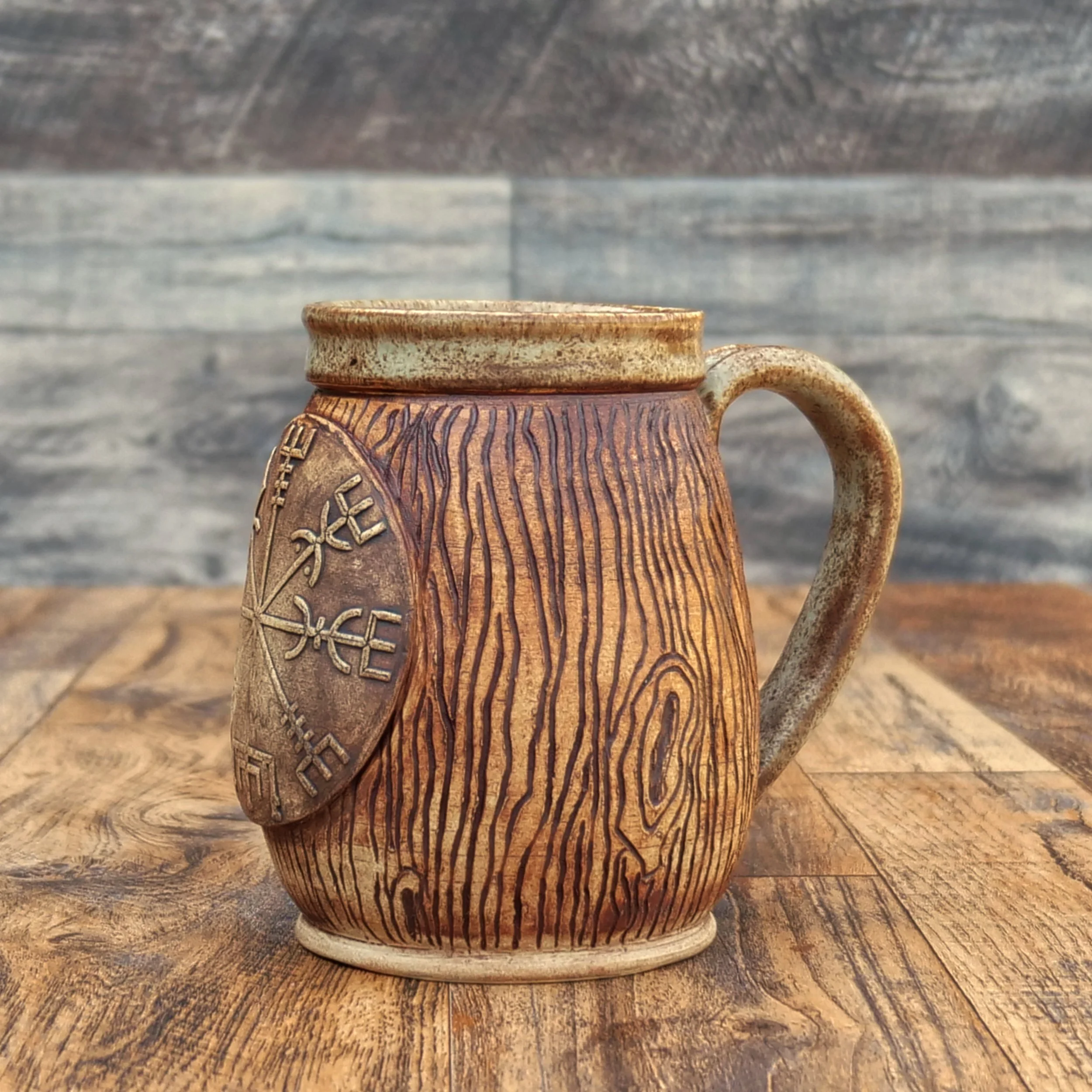Handmade stoneware Wayfinder Mug by Elderkiln Ceramics featuring a raised Vegvísir symbol, hand-carved woodgrain texture, and warm earth-tone glazes.