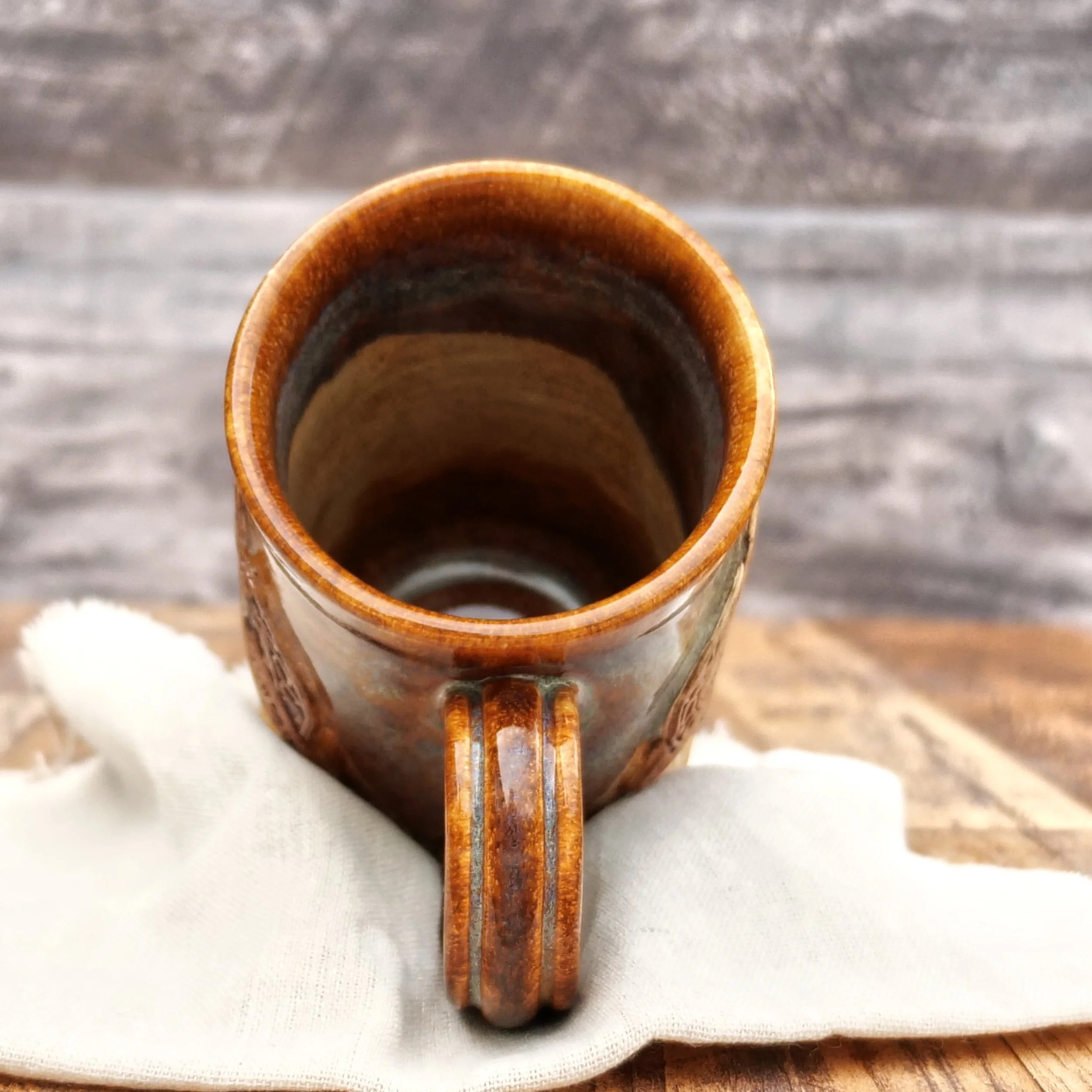 Handmade Trinity Knot Mug by Elderkiln Ceramics featuring a sculpted Celtic knot design and layered earthy brown and mineral-toned stoneware glazes.