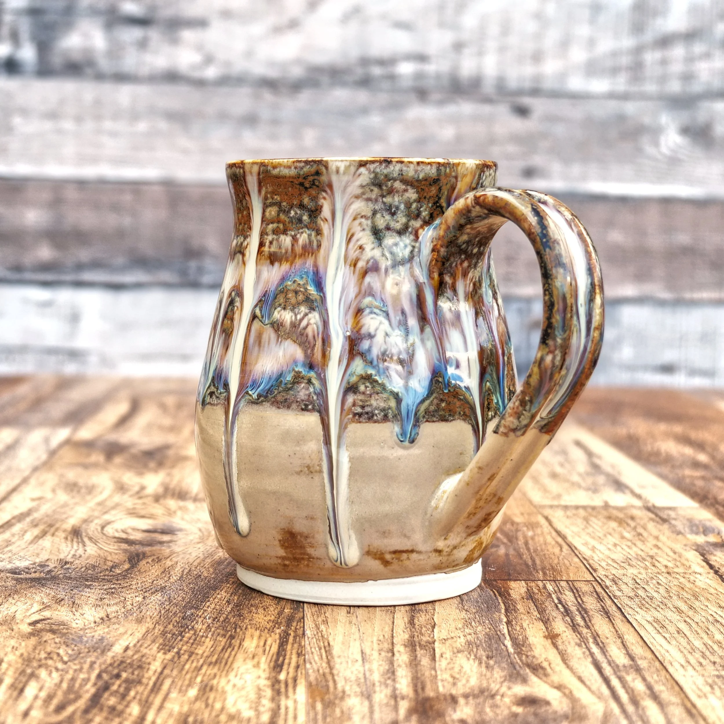 Handmade stoneware Cascade Mug by Elderkiln Ceramics featuring flowing layered glazes in earthy brown, cream, and mineral tones on a rustic pottery mug.