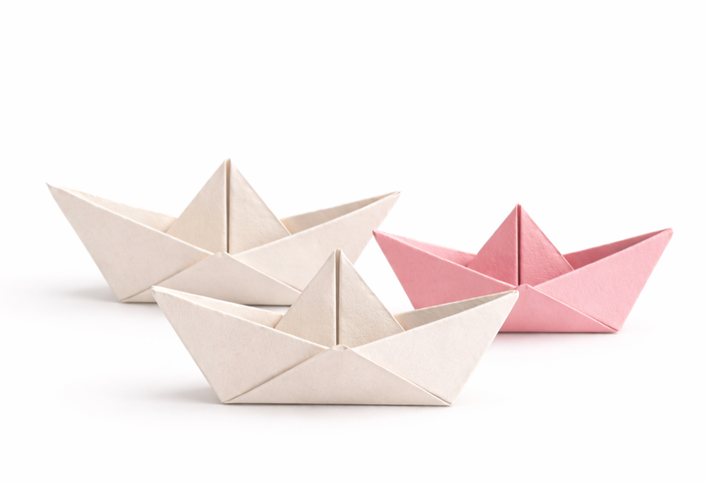 Three paper origami boats, two white and one pink, arranged on a white background.