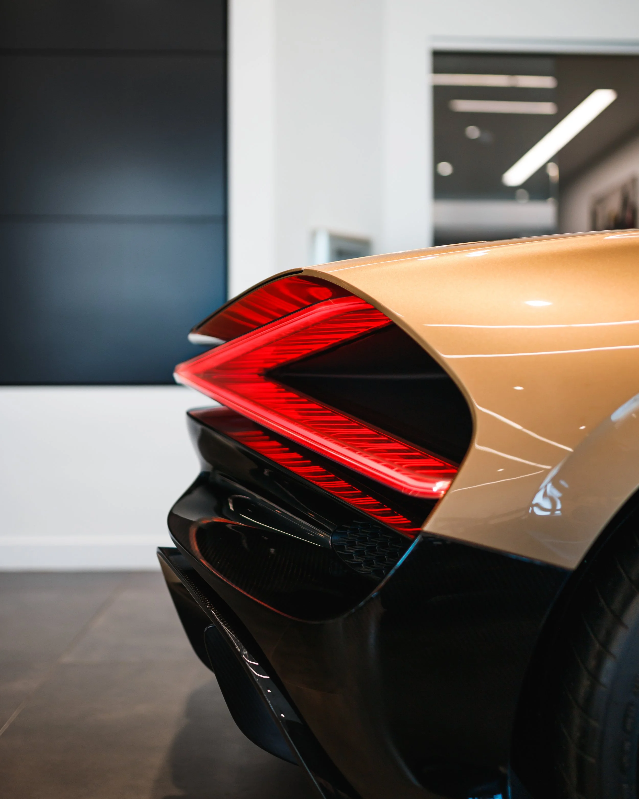 Close-up of a Bugatti Mistral's rear end, featuring a sleek gold and black design with prominent red tail lights.