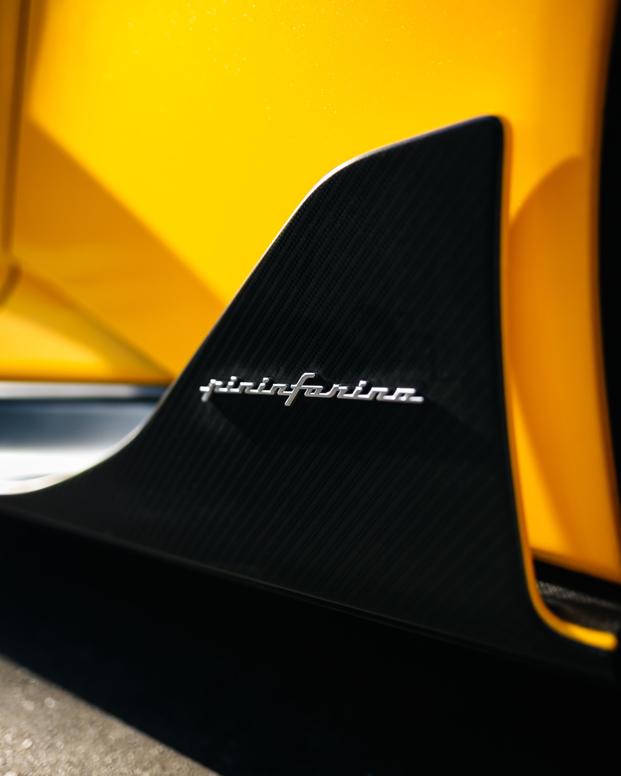 Close-up of a yellow Pininfarina Battista featuring a black rear wing with a silver 'Pininfarina' badge.