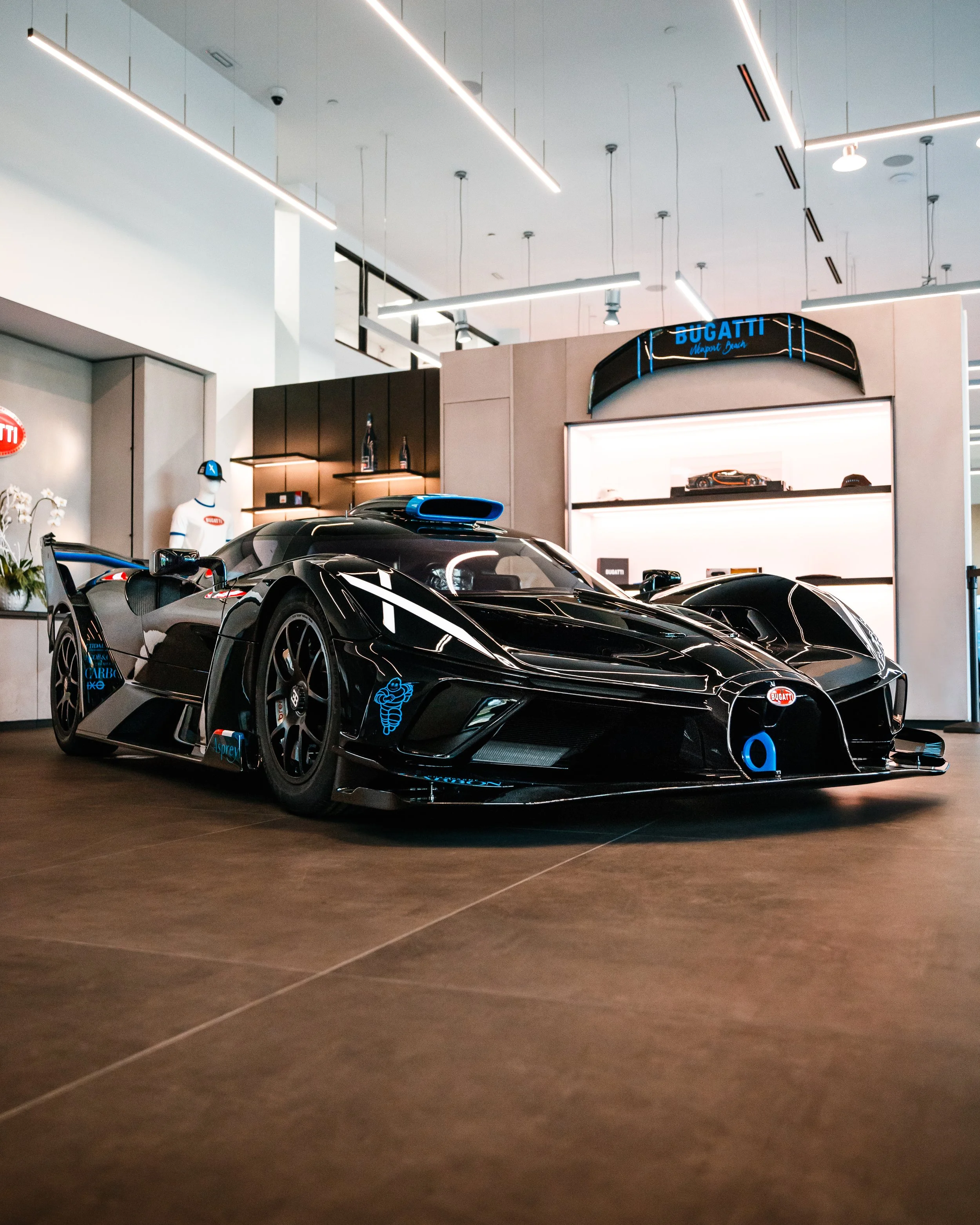 A black Bugatti Bolide inside a showroom with display shelves and a white mannequin in the background.