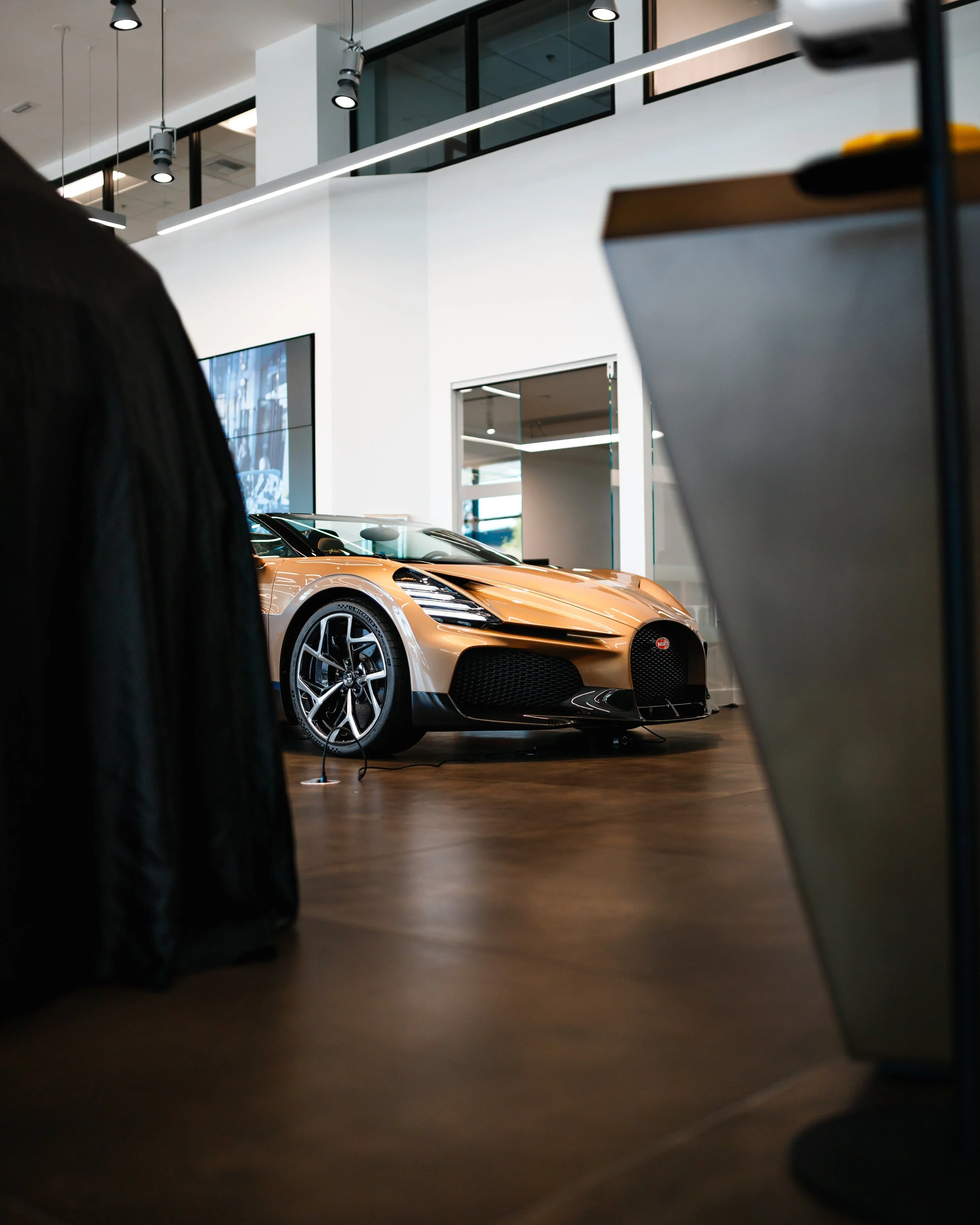 A Bugatti Mistral in a showroom, with modern white walls, large glass windows, and ceiling lights.
