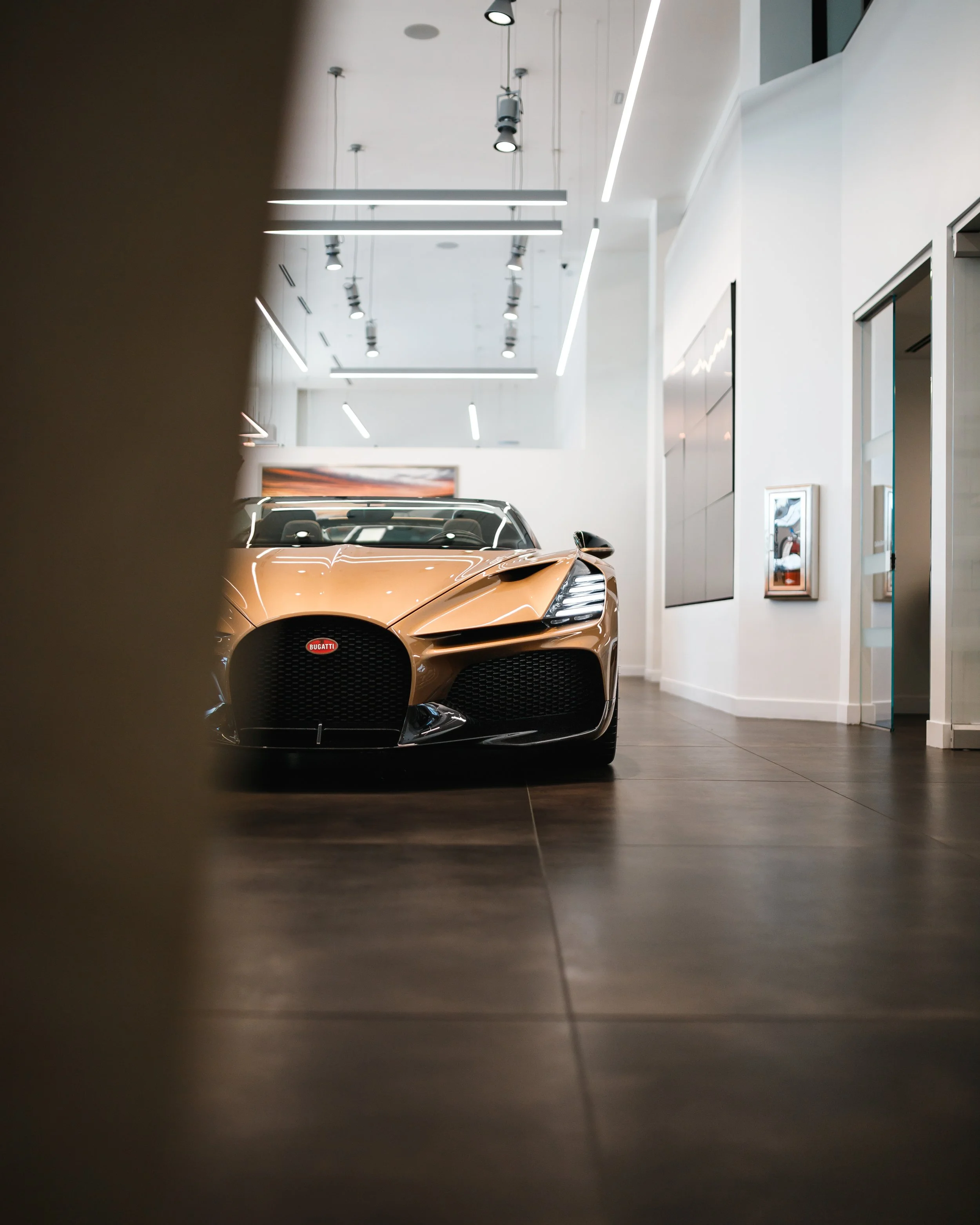 A Bugatti Mistral displayed in a modern showroom with white walls, dark flooring, and ceiling lights.