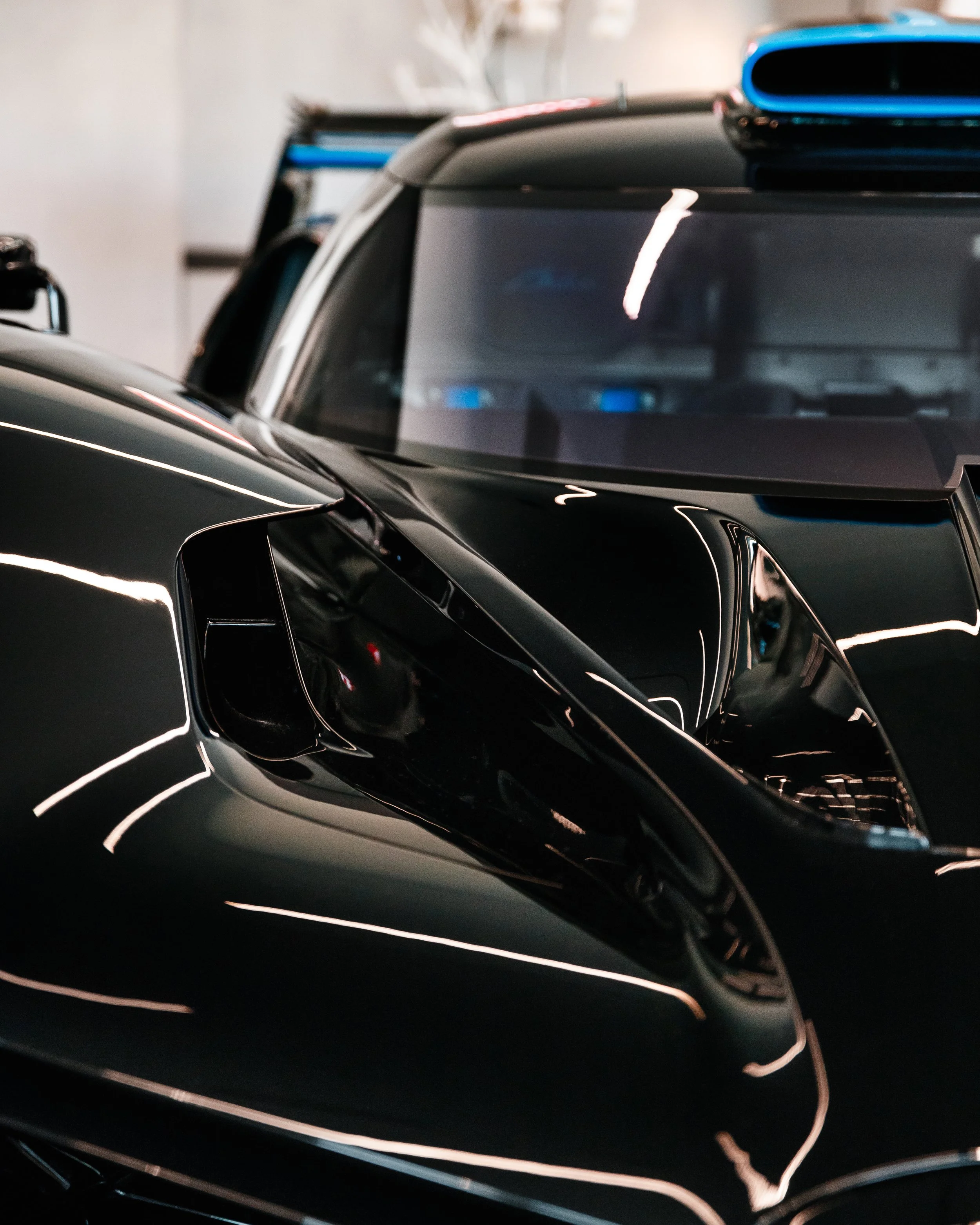 Close-up of the front part of a sleek, black Bugatti Bolide with shiny paint, showing its angular headlight and aerodynamic curves.