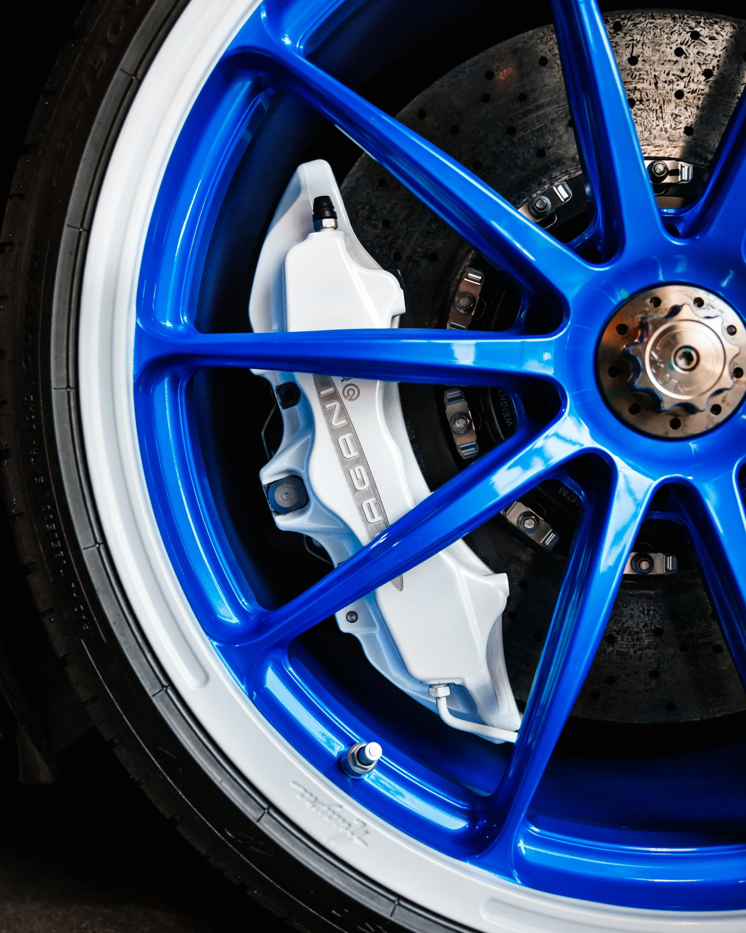 Close-up of a Pagani Huayra wheel with a white brake caliper labeled 'PAGANI' and a drilled brake rotor.