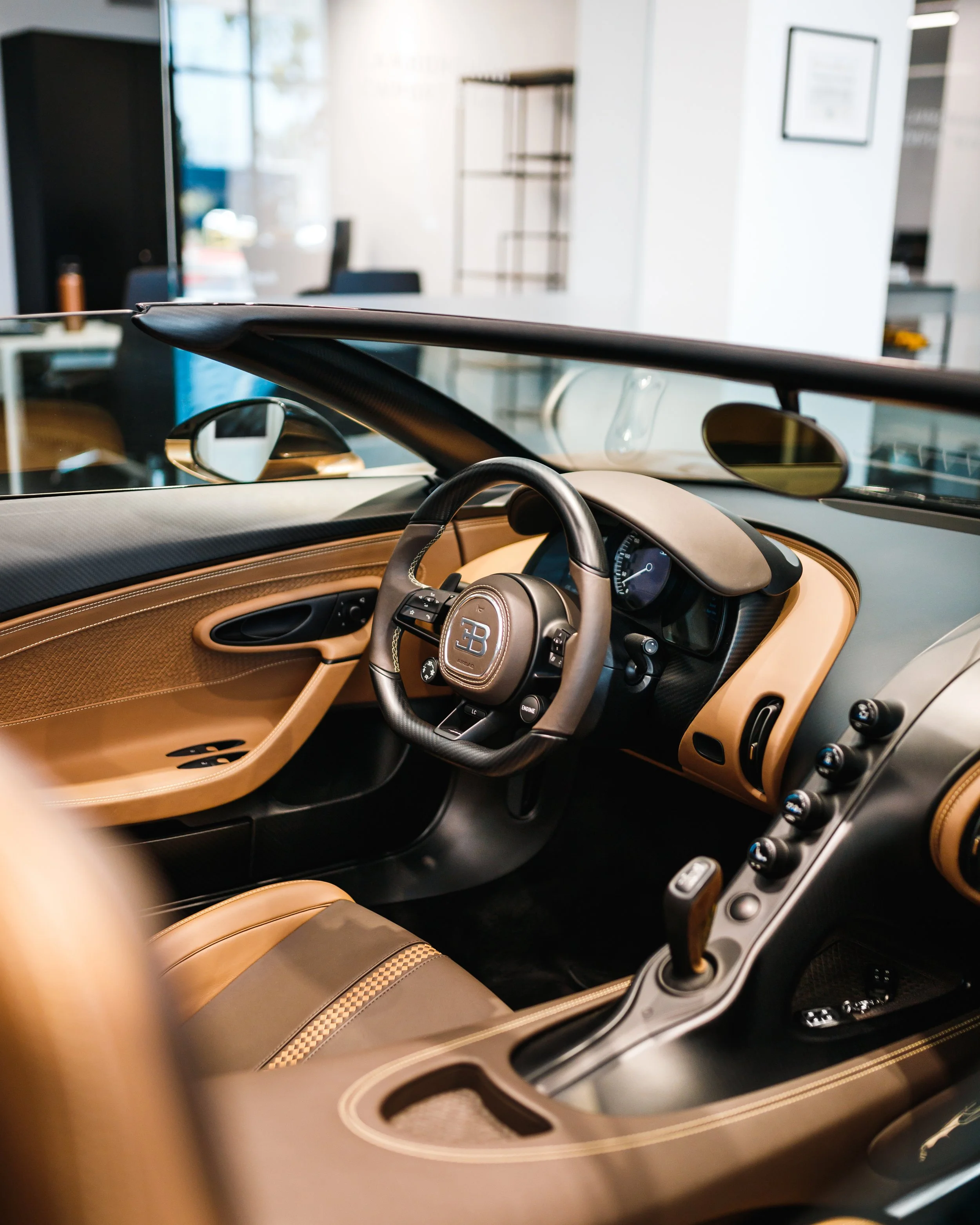 Interior of a Bugatti Mistral showing the steering wheel, dashboard, tan leather seats, and gear shift.