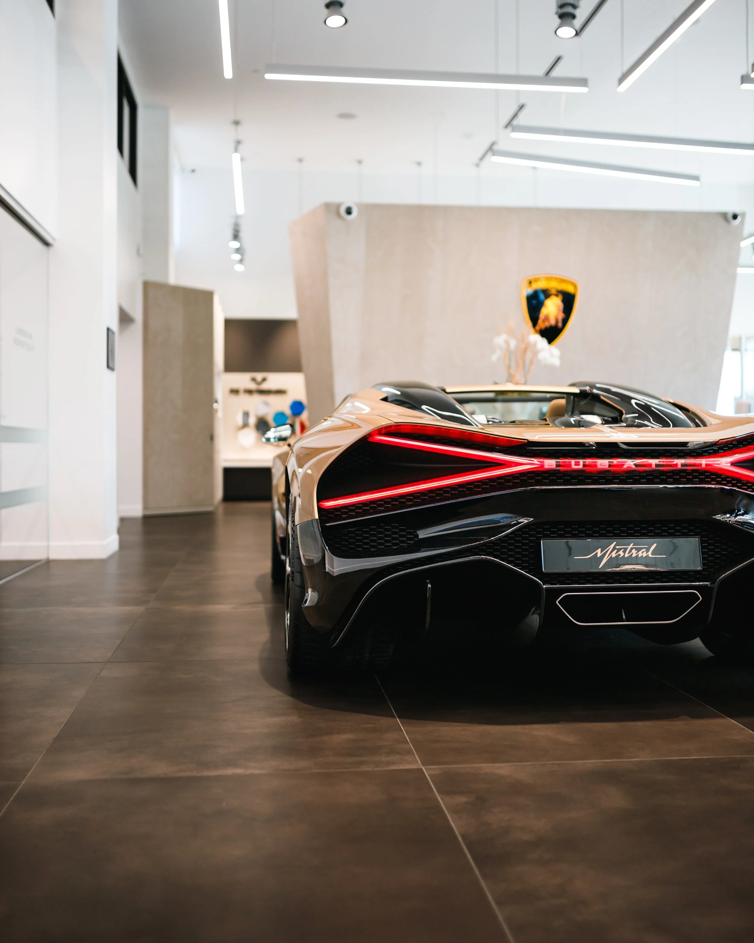 ABugatti Mistral displayed inside a modern showroom, with a Lamborghini badge visible on a wall in the background.