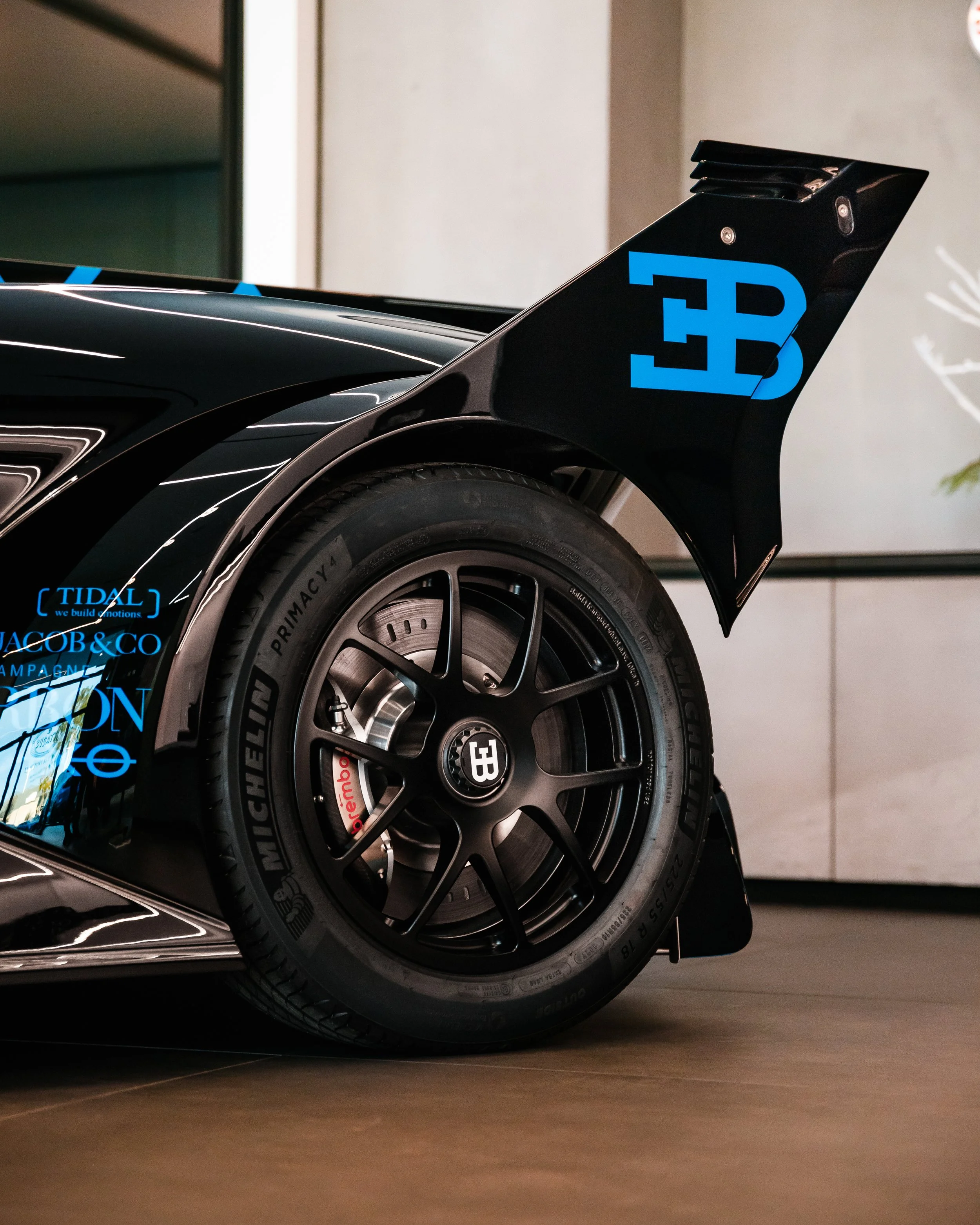 Close-up of a black Bugatti Bolide, focusing on the rear wheel with Michelin tires and the rear wing with the Bugatti logo in blue.
