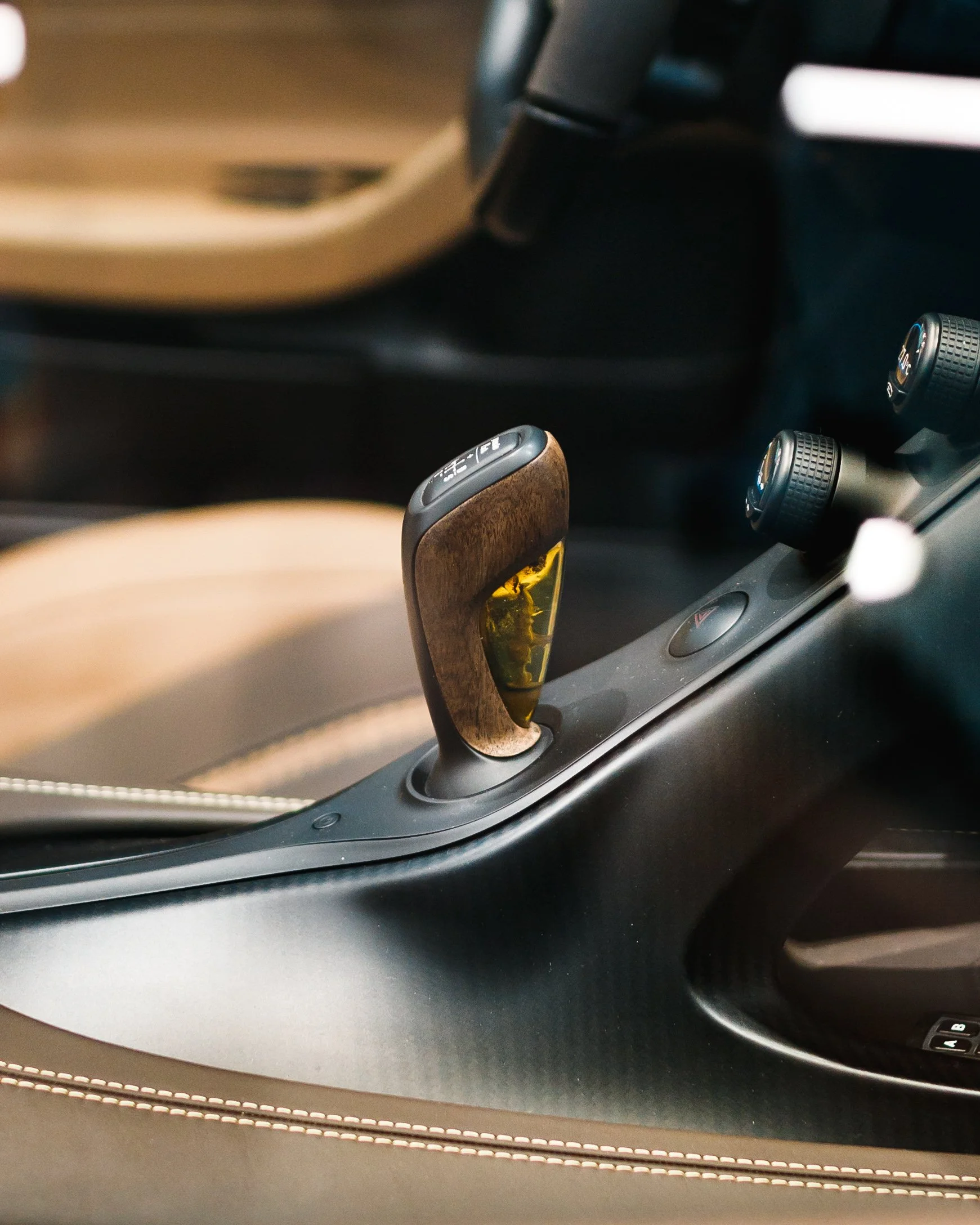 Close-up of a Bugatti Mistral's gear shift lever with a wooden and black design, located in the center console of the vehicle.