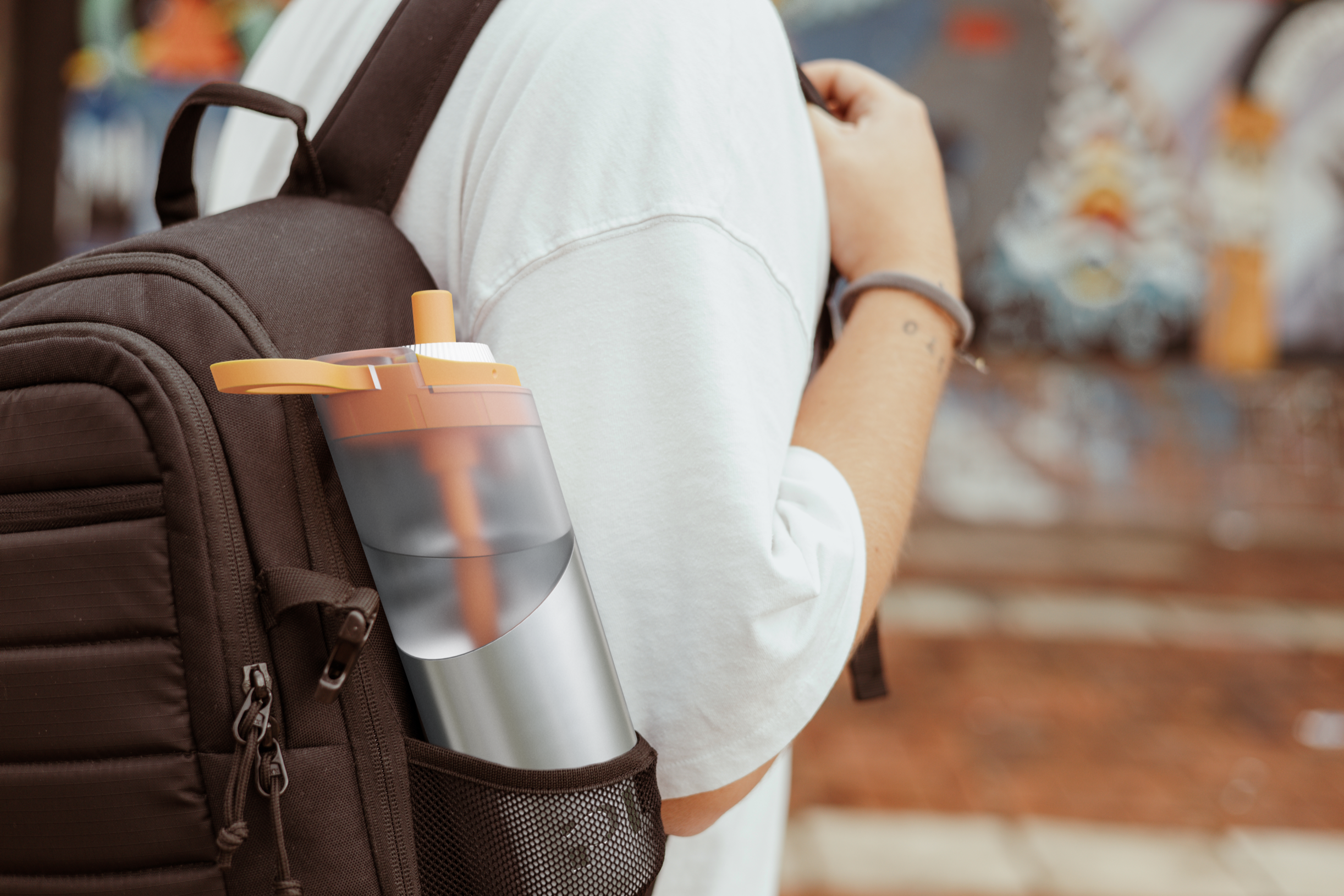 A person wearing a white t-shirt with a backpack that has a CGI water bottle in the side pocket added digitally, holding the strap of the backpack in an outdoor setting.