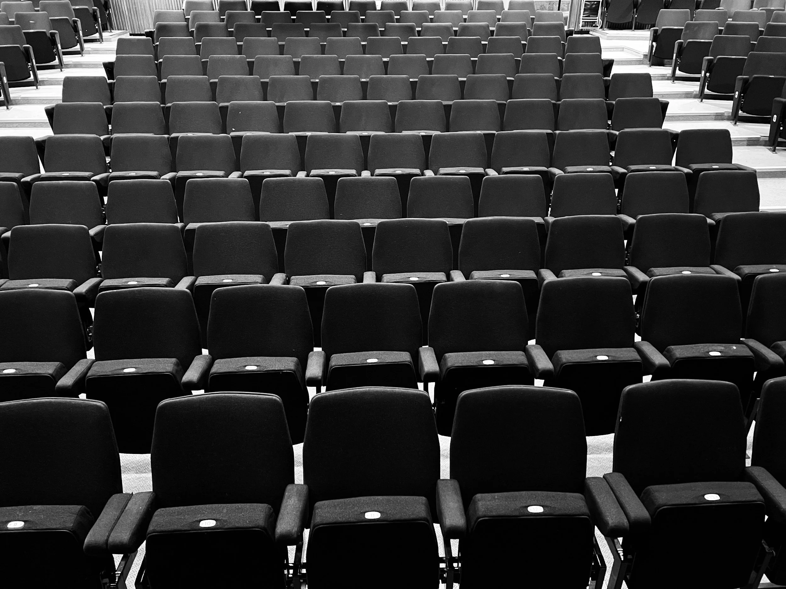 Empty theater or auditorium with multiple rows of black chairs.