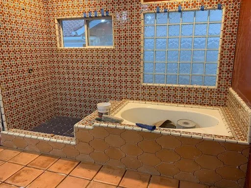 Bathroom with a built-in bathtub, tiled walls with colorful geometric patterns, glass blocks, and two small windows.