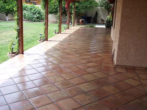 Covered porch with terracotta tiles, wooden support beams, adjacent lawn, and garden in the background.