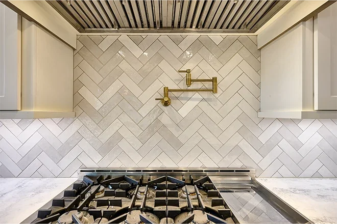Kitchen stove with a herringbone tile backsplash and a gold faucet on the wall.