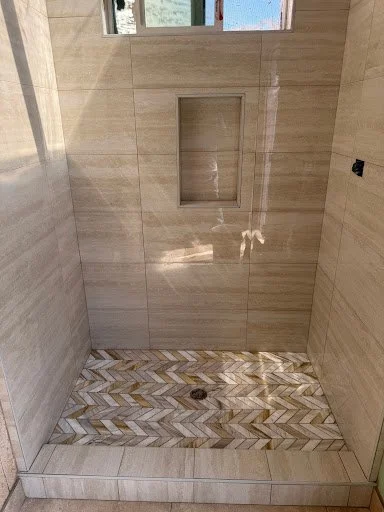 Bathroom shower with beige tile walls, a built-in niche for toiletries, and a chevron-patterned tile floor.
