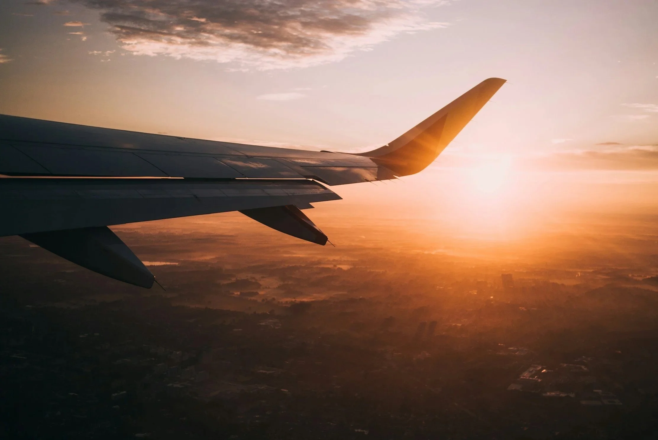 The wing of an airplane flying at sunset photographed from within the plane.