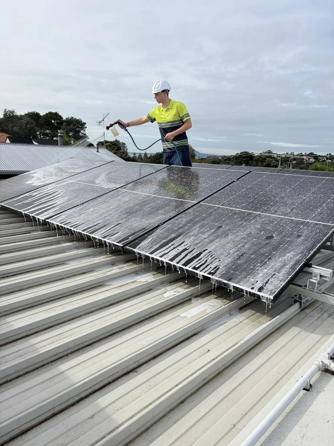 A worker in safety gear is spraying down solar panels with a solution.