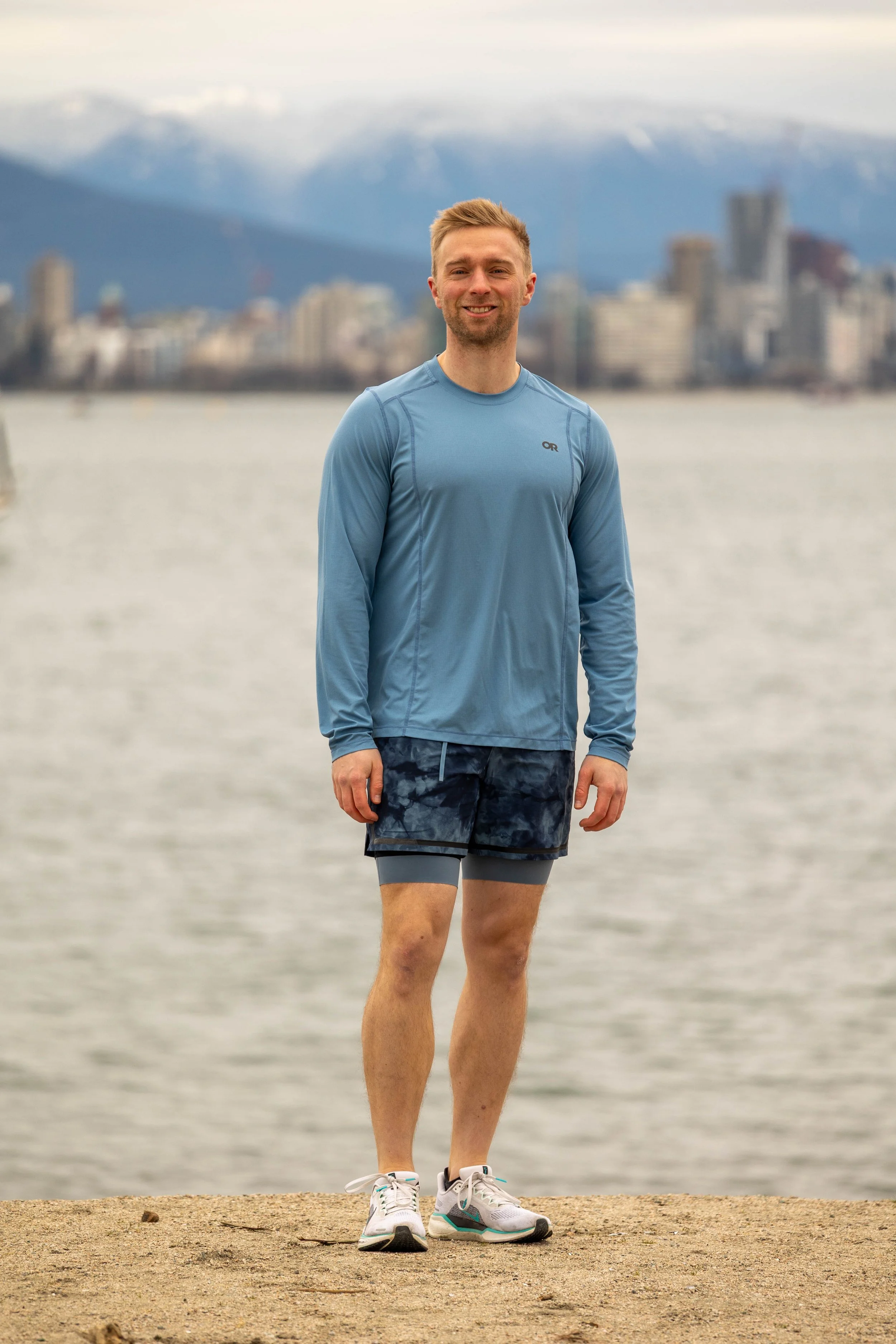 Personal trainer smiling on the beach with the Vancouver skyline and mountains in the background