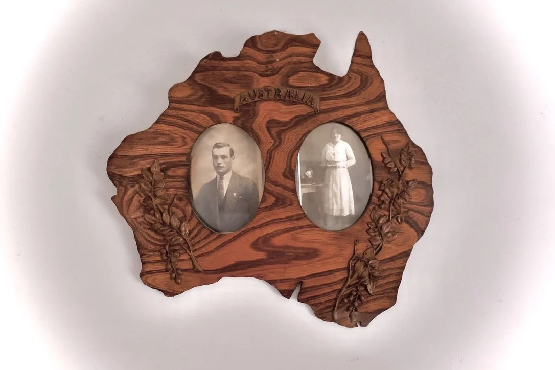 Wooden picture frame in the shape of Australia with two vintage black-and-white photographs of a man and a woman, and the word 'Australia' carved at the top.