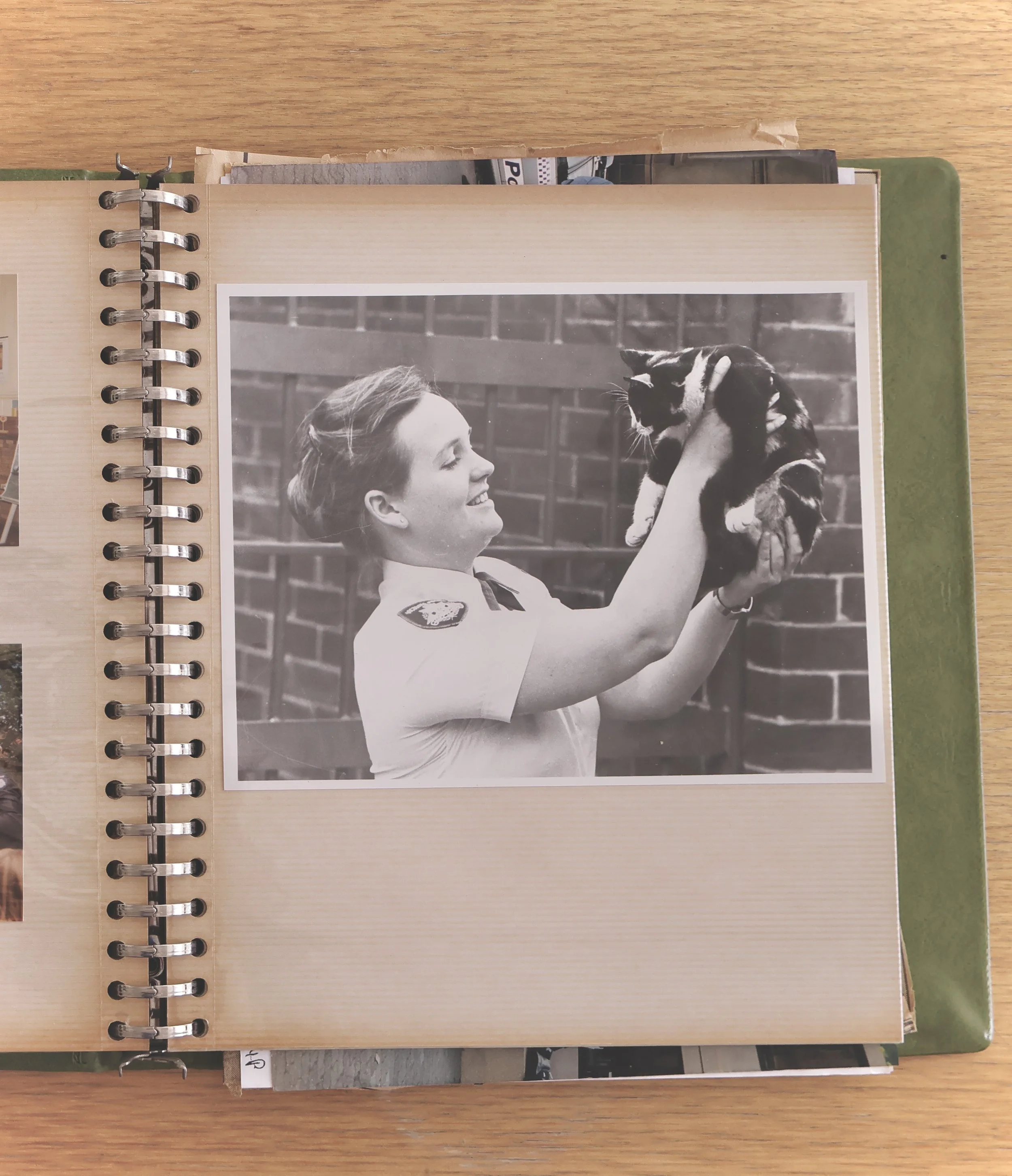 A black and white photograph of a woman holding a kitten in front of a brick wall.