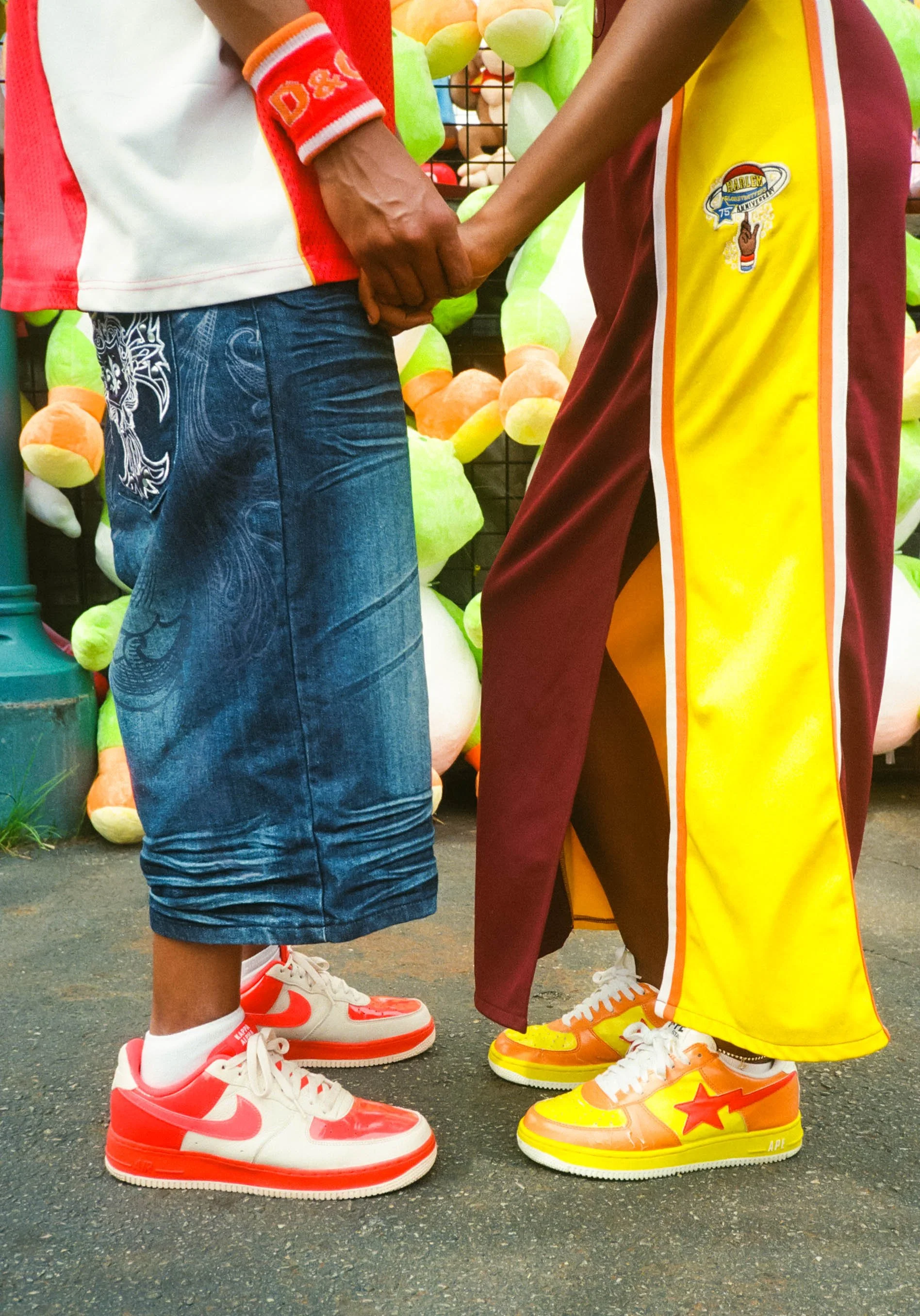 Close-up of two people holding hands, wearing colorful sneakers and clothing, standing outdoors on pavement.