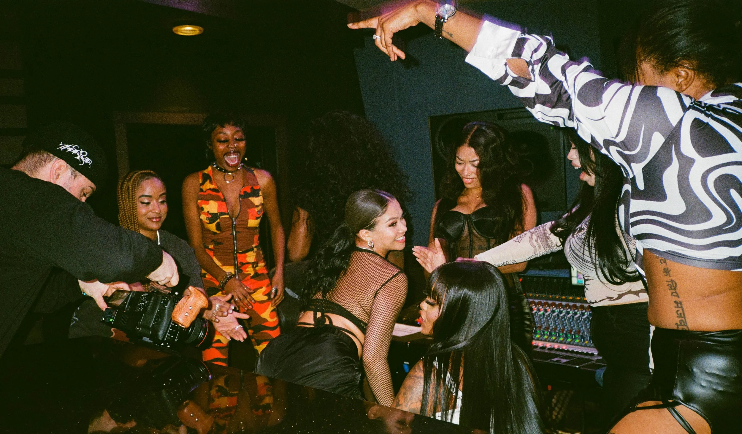 Group of diverse women and men in a recording studio, engaged in a lively discussion or celebration around a mixing console.