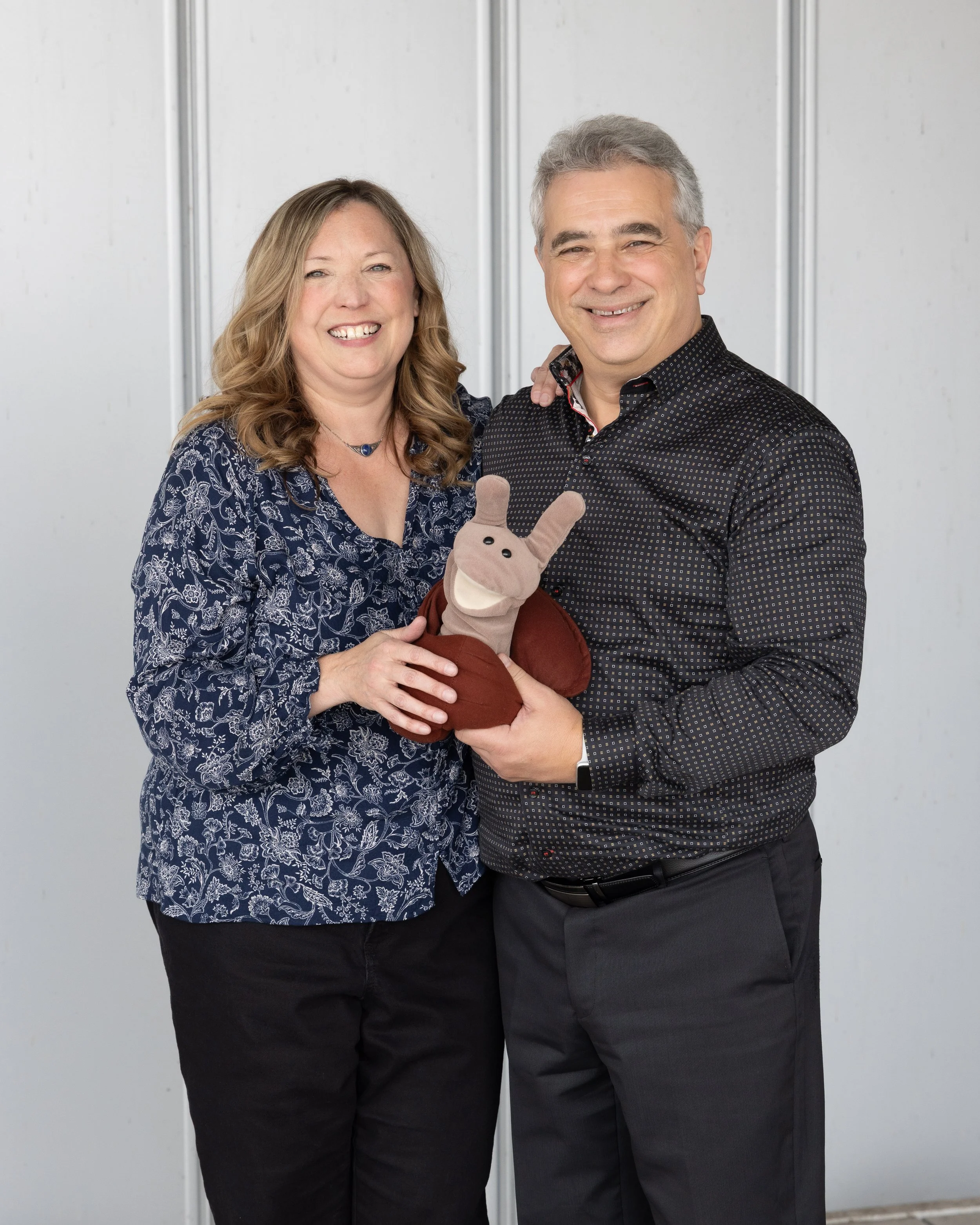 Un homme et une femme souriants, devant un fond neutre, avec un objet en forme de lapin en peluche dans les mains de l'homme
