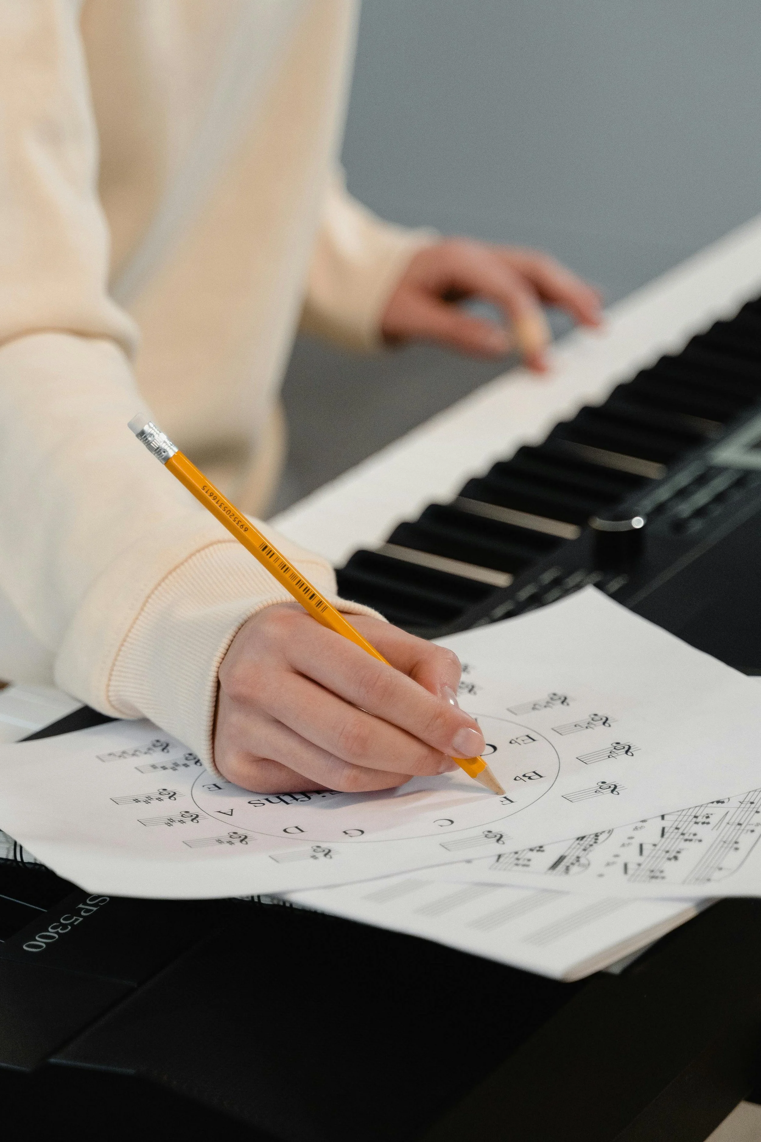 Une personne écrit des notes musicales sur une feuille de papier avec un crayon jaune, près d'un piano noir.