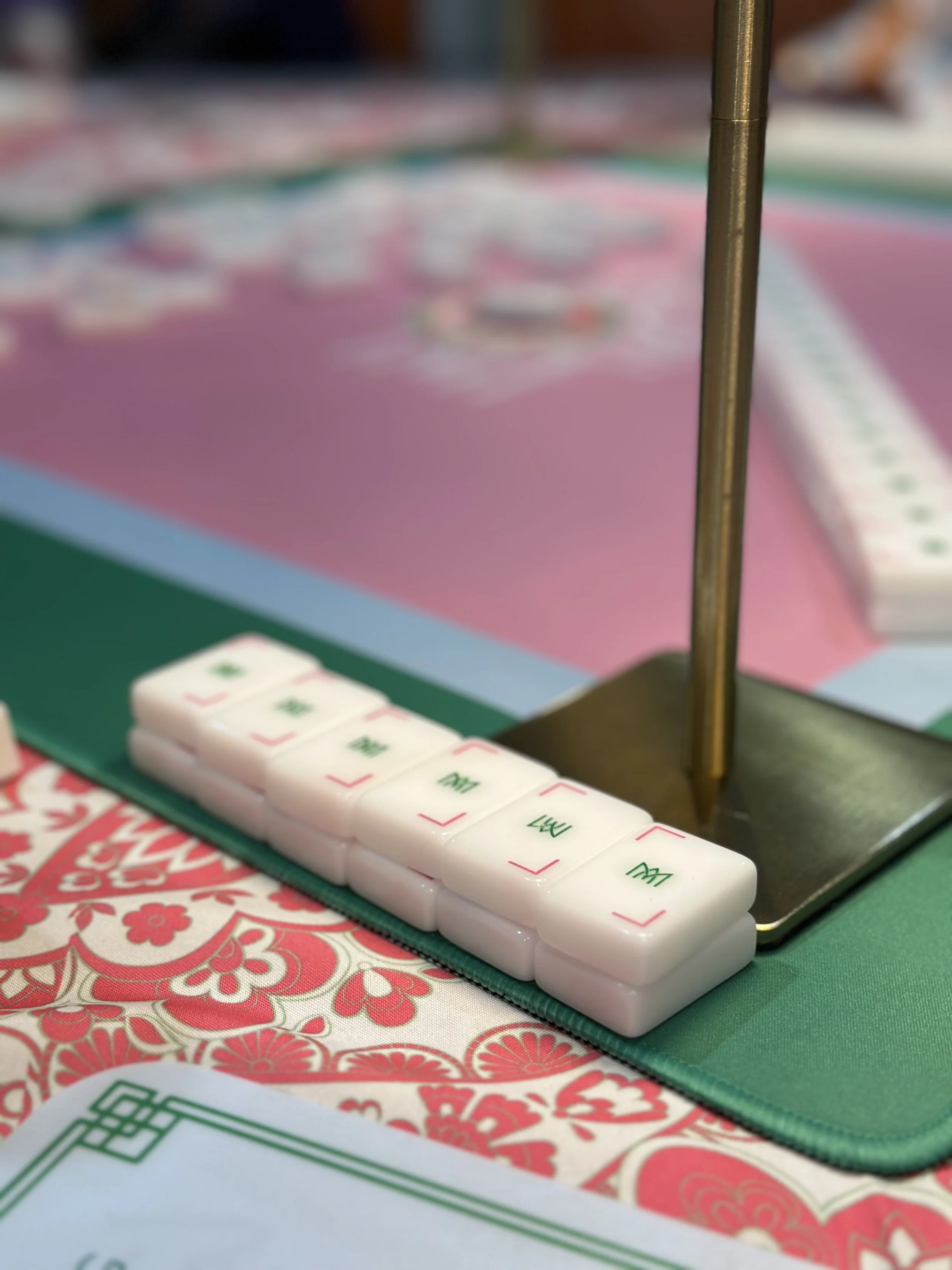 Close-up of mahjong tiles on a colorful table with a green mat and pink playing surface.