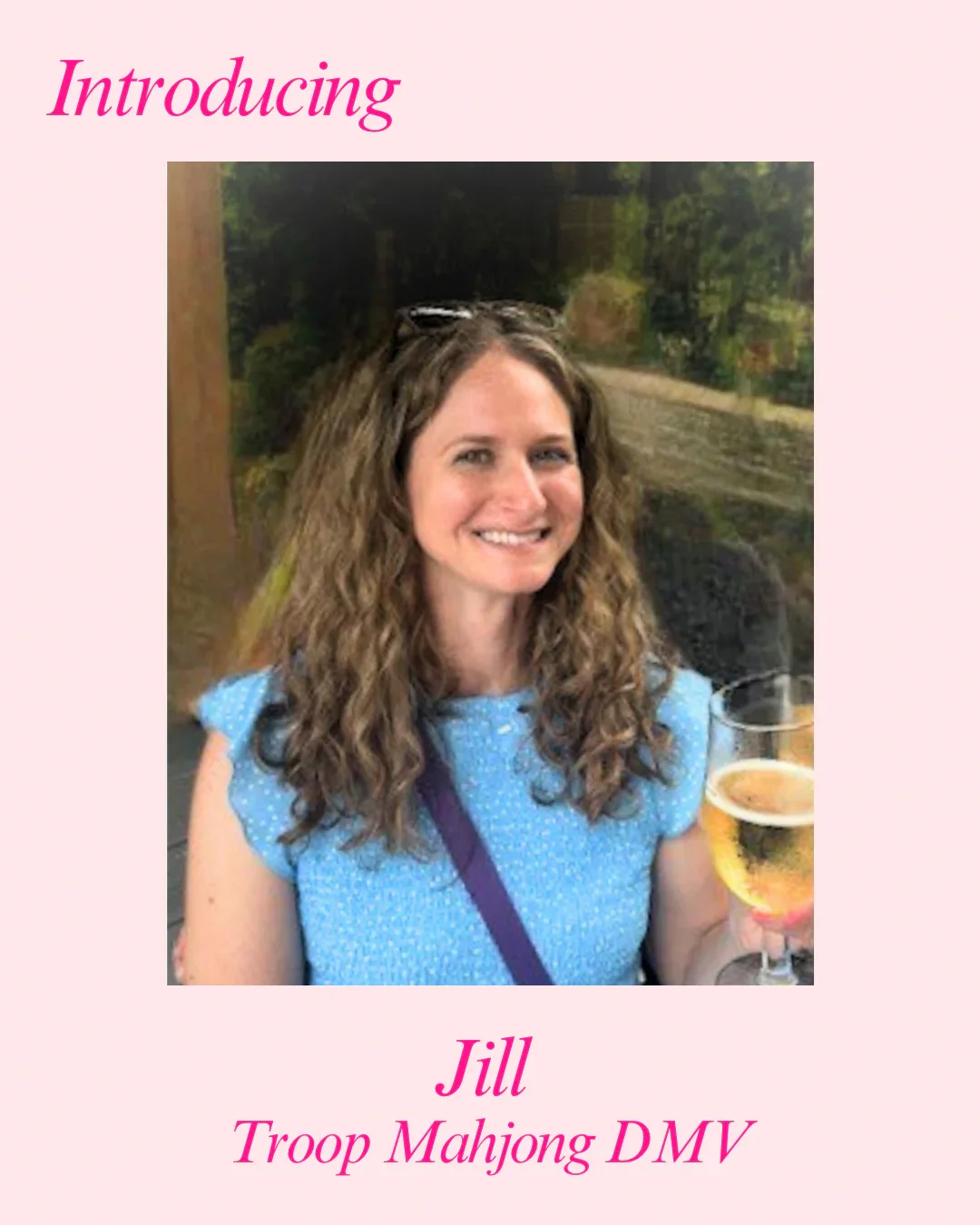 A smiling woman with curly brown hair holding a glass of white wine, wearing a blue polka dot top, with text introducing Jill from Troop Mahjong DMV.
