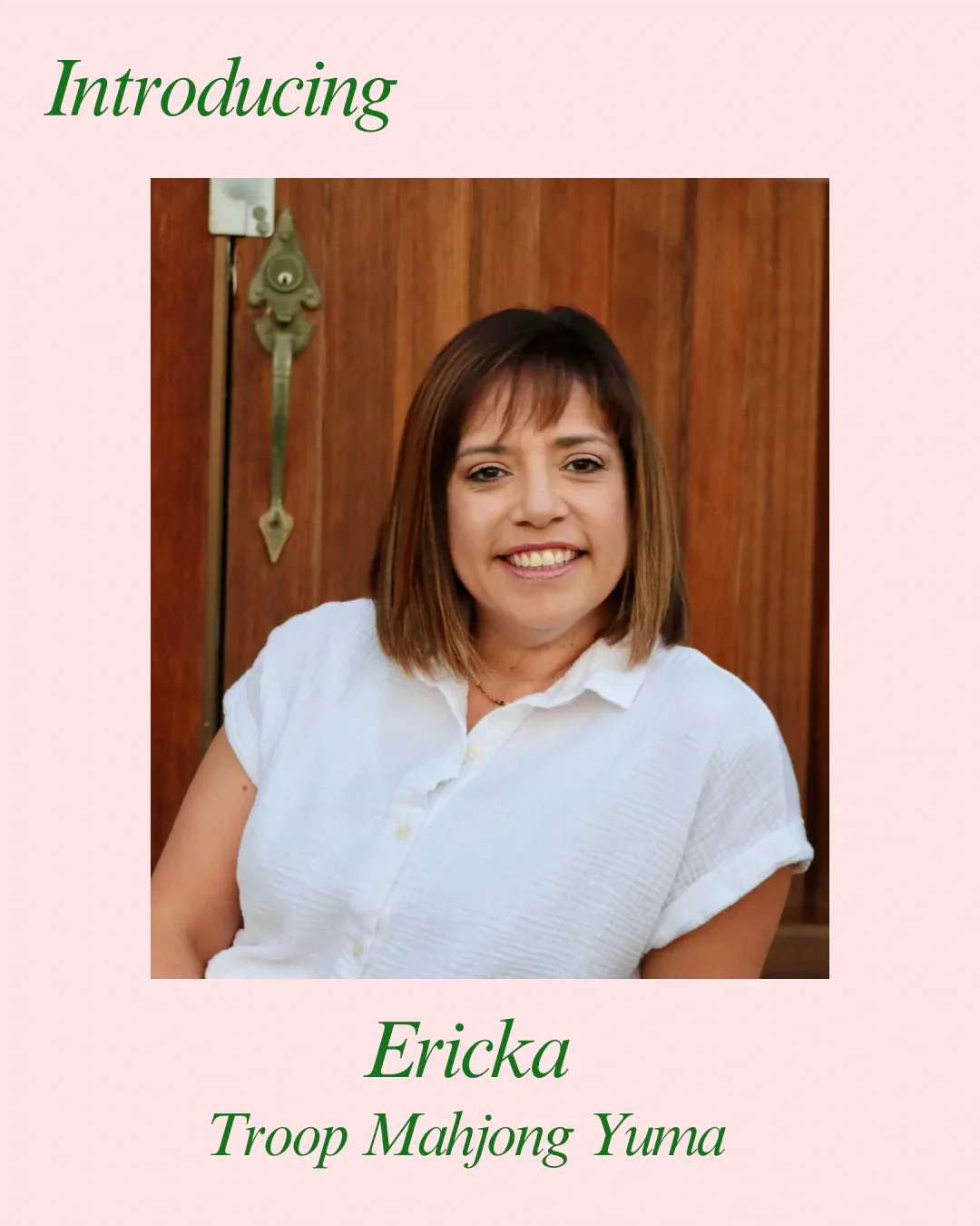 A woman with shoulder-length brown hair smiling, wearing a white button-up shirt, standing in front of a wooden door.