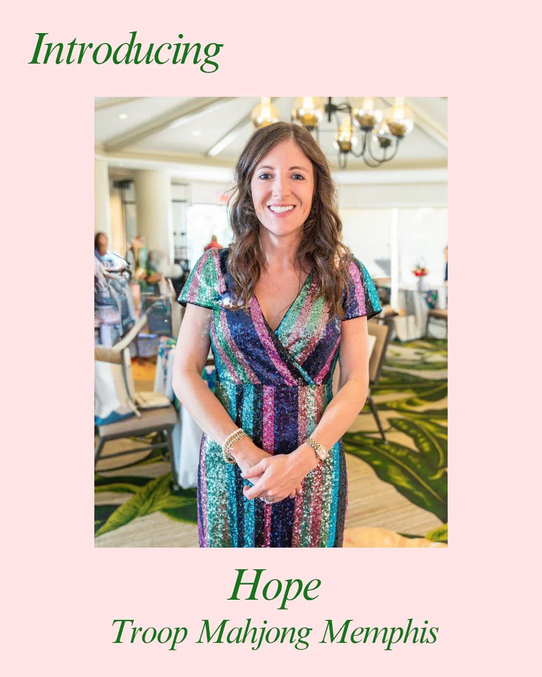 A woman with brown curly hair smiling, wearing a colorful striped sequin dress, standing in a well-lit indoor setting with people and tables in the background.