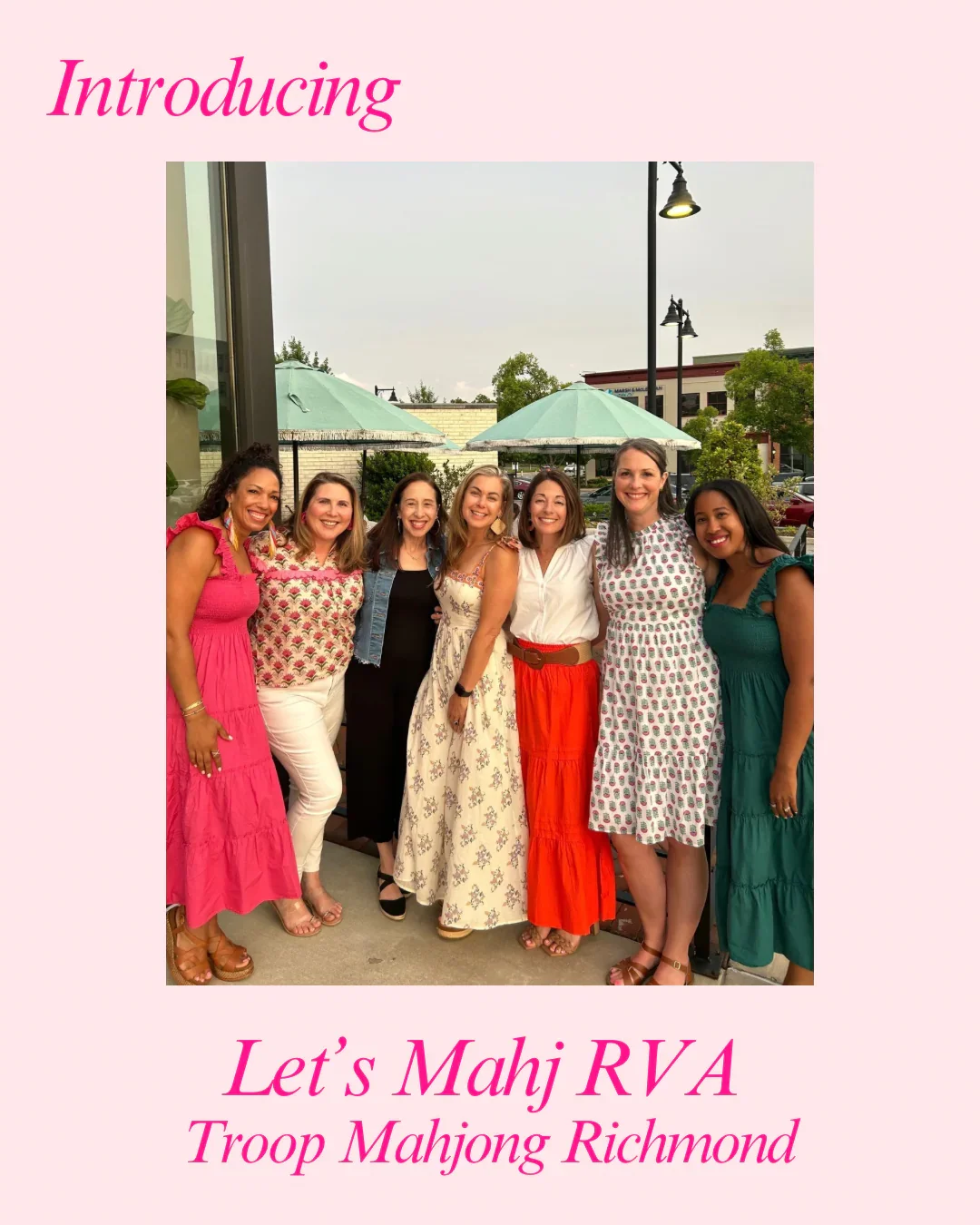 A group of seven women standing outdoors under umbrellas, posing for a photo with trees and a city street in the background.