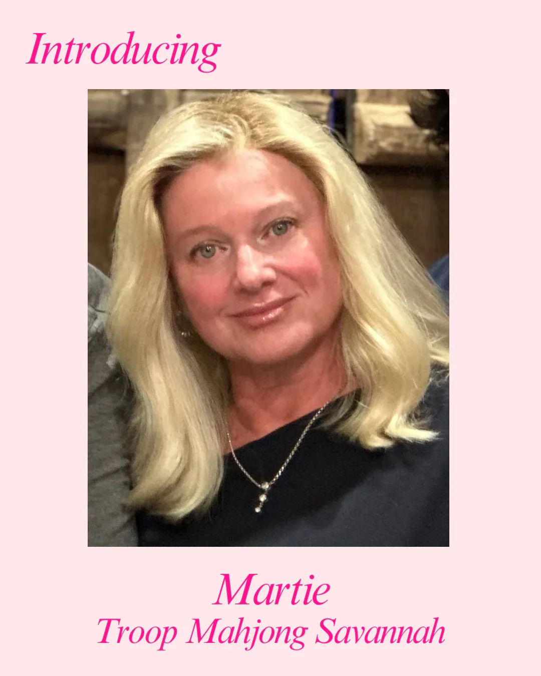 A woman with blonde hair and a black top, smiling, wearing a necklace, in front of a wooden background with pink text that says 'Introducing Martie Troop Mahjong Savannah'.