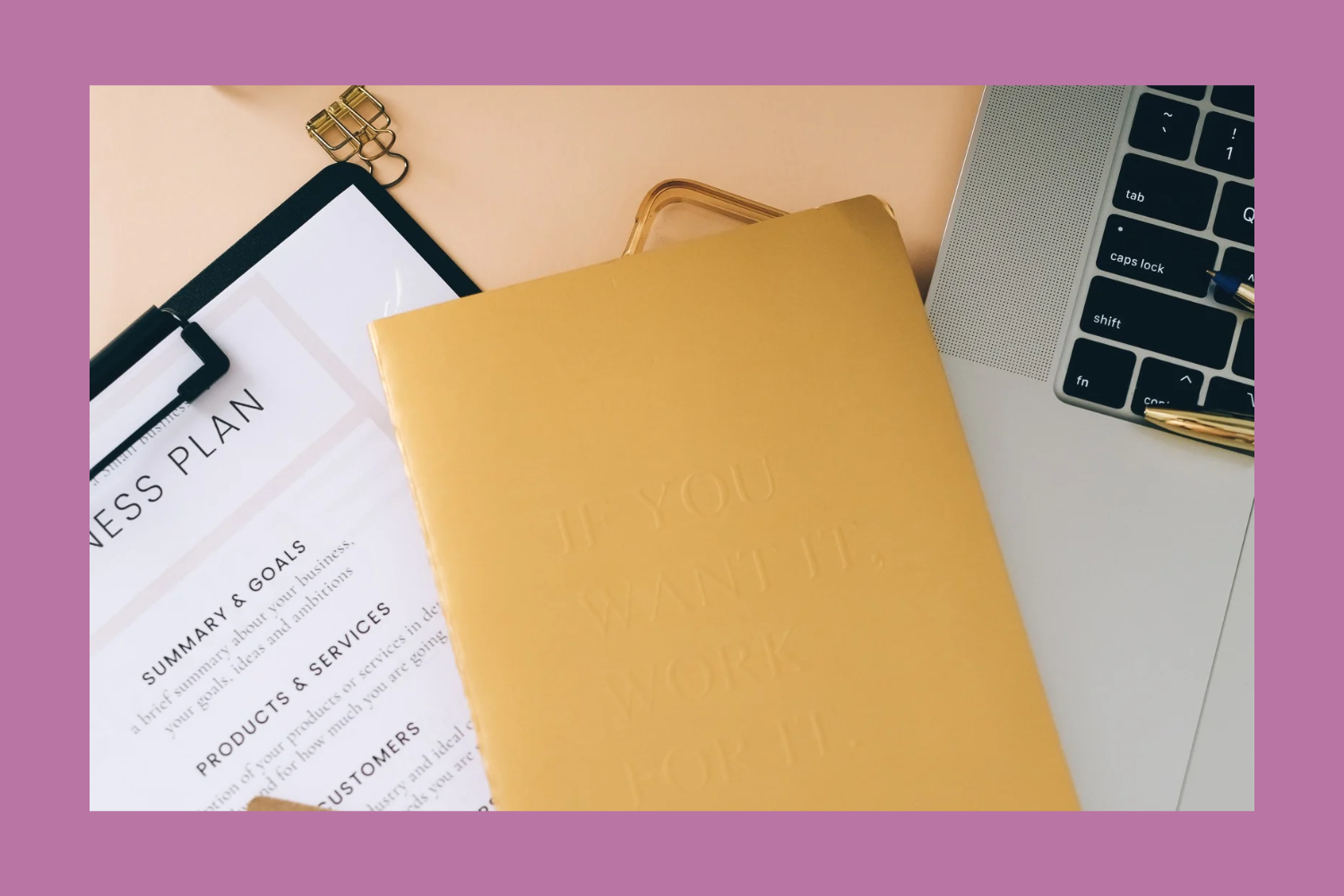 A flat lay of office items including a notebook with a yellow cover, a business plan document on a clipboard, and part of a laptop keyboard, on a pink background.