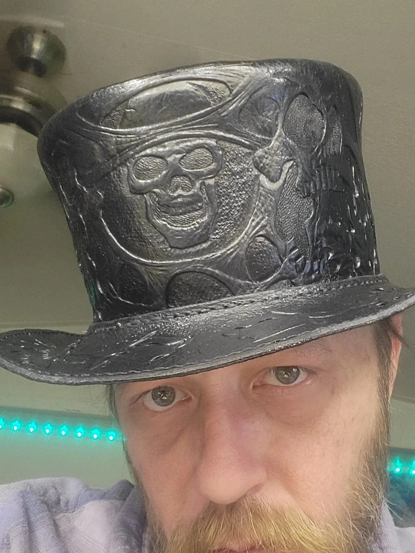 A man with a beard wearing a shiny black top hat with skull and skeleton designs.