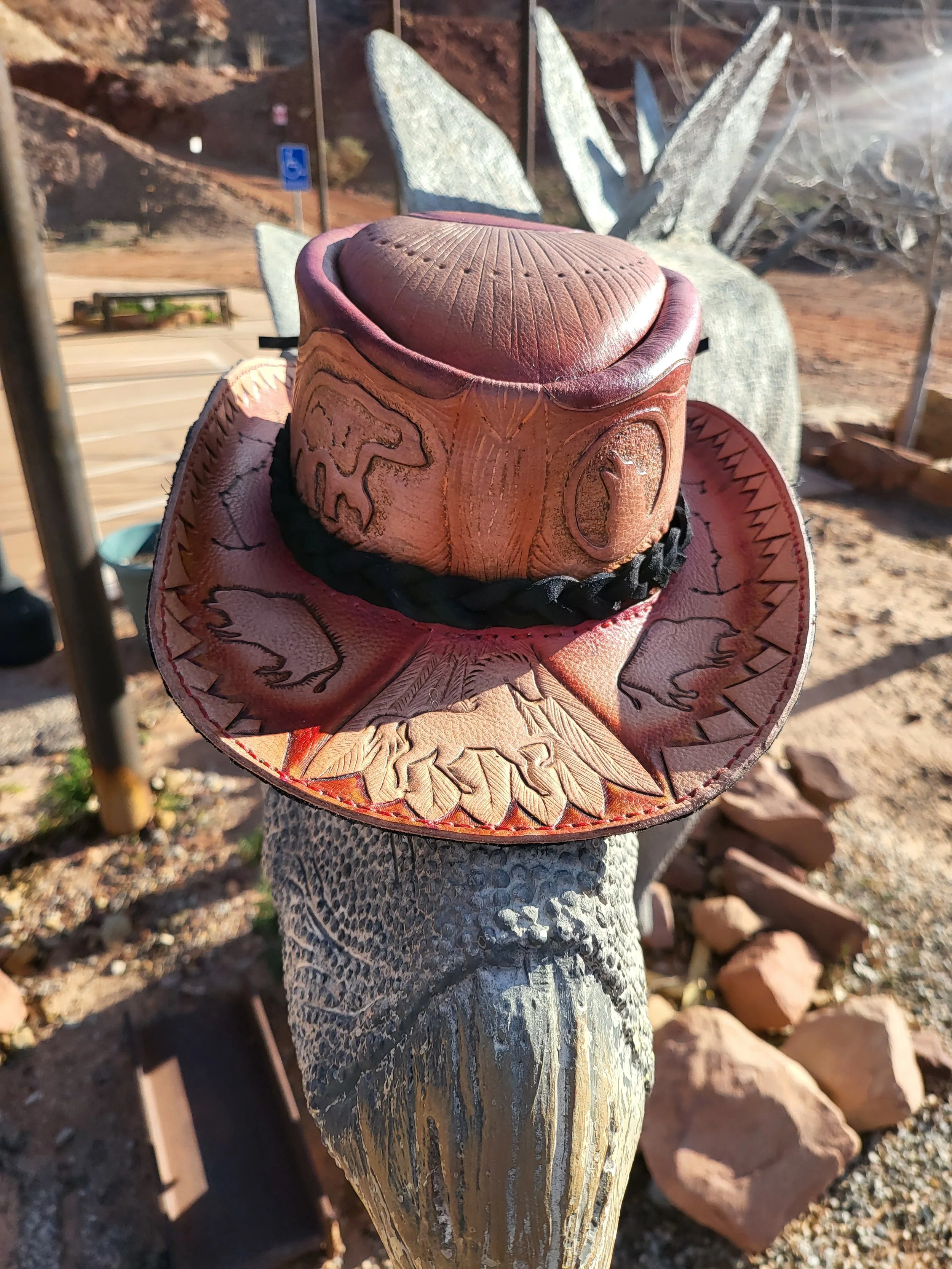 A decorative cowboy hat with embossed animal designs, placed on a weathered wooden post.