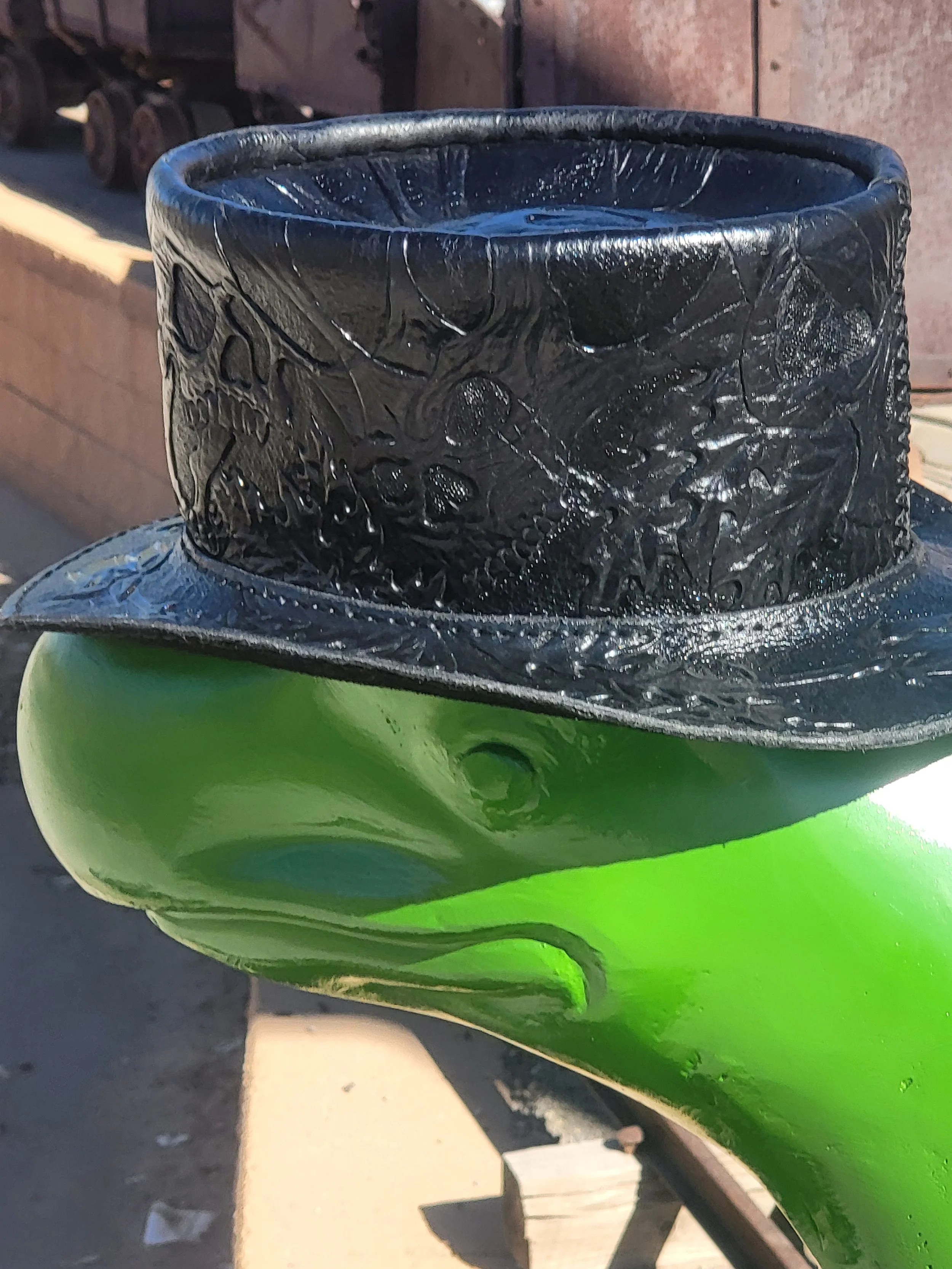 Close-up of a green painted metal sculpture with a black carved top, outdoors on a sidewalk.