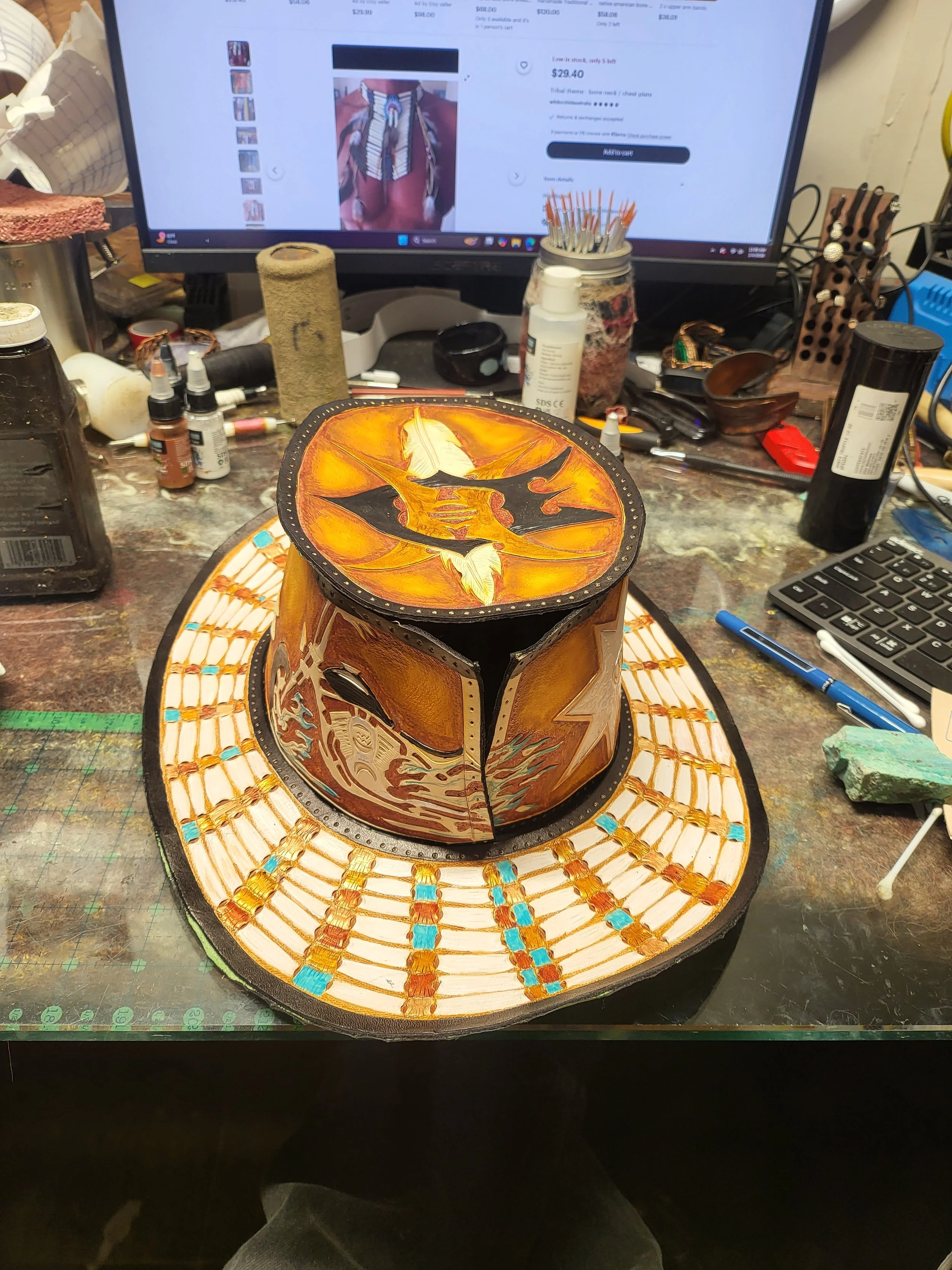 A painted pot decorated with Batman and other comic-themed designs, placed on a colorful woven mat on a cluttered workspace.