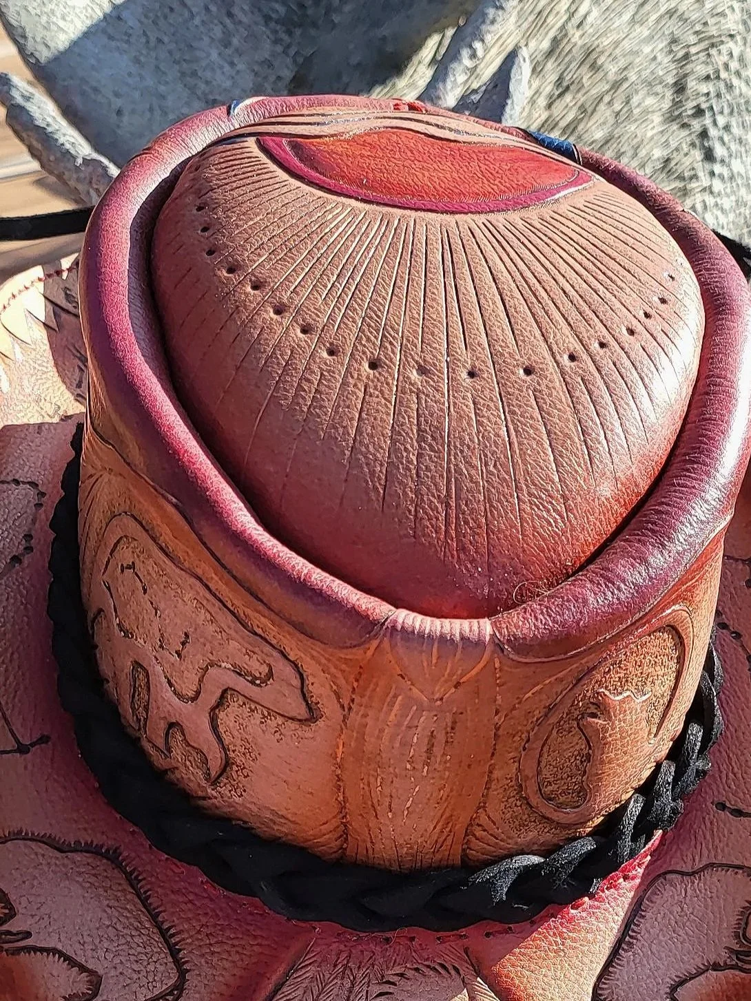 Leather cowboy hat with decorative tooled leather band and stitched brim, resting on a rock.