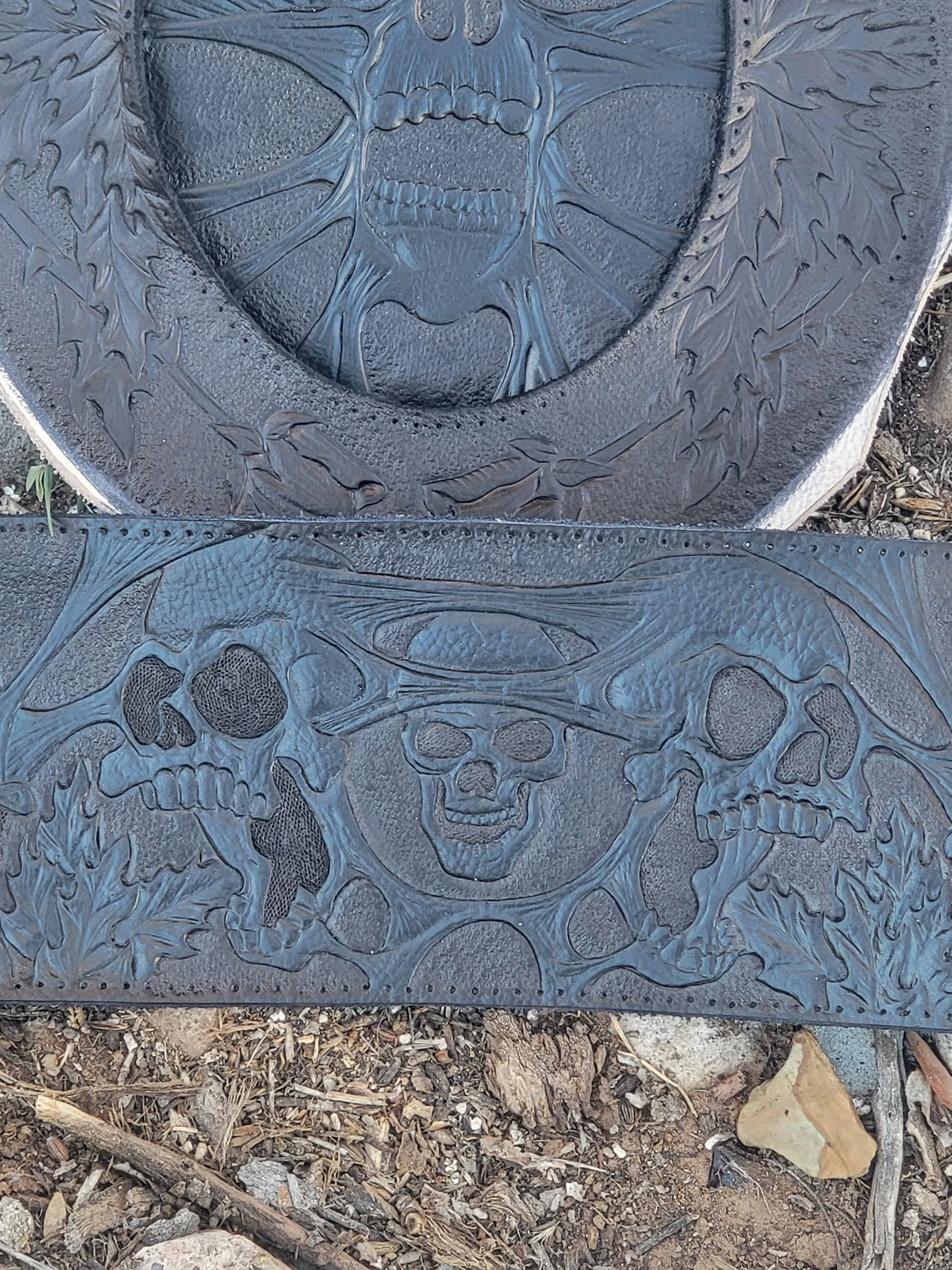 Decorative metal plaque with skulls, a hat, and leafy designs.