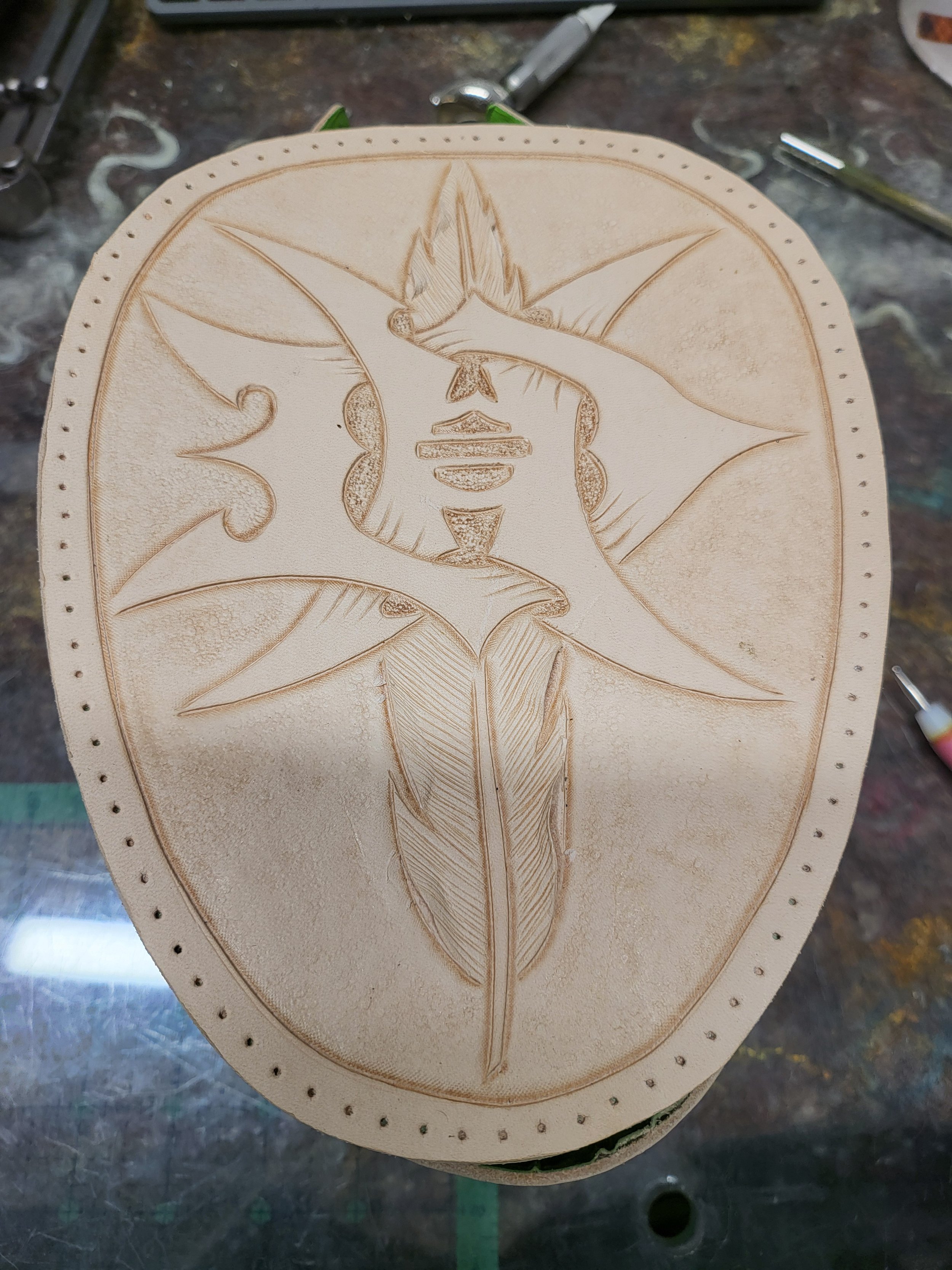 Wooden carving of a face with leaves as hair, with detailed line work, on a rounded rectangular piece of wood.