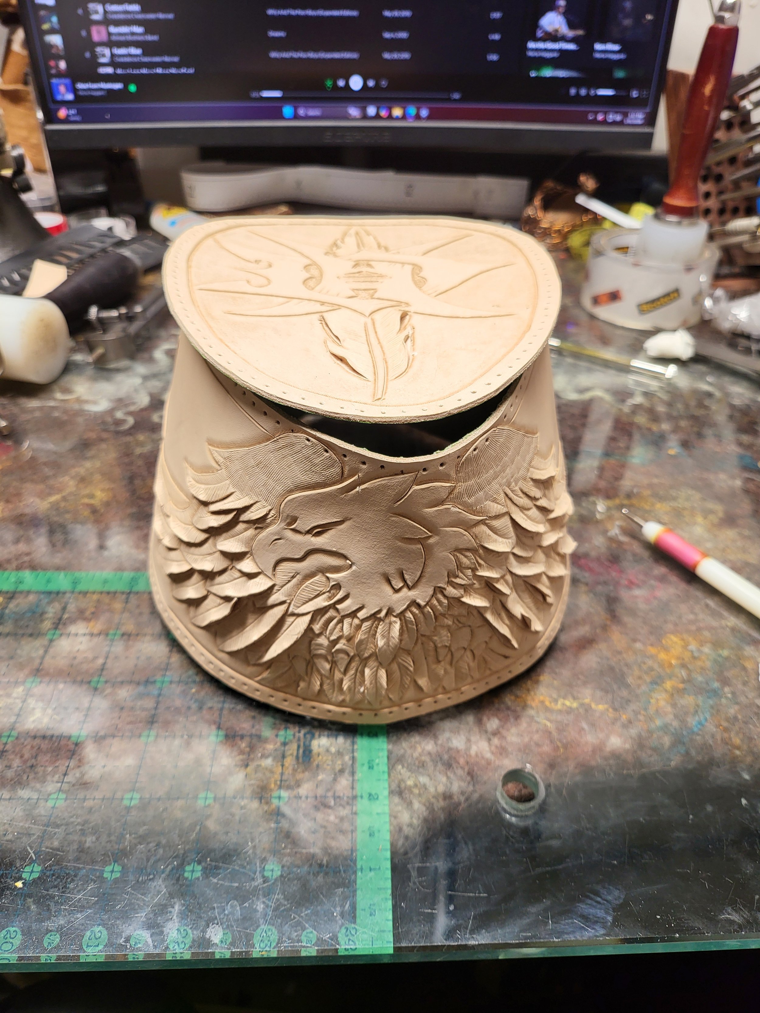 Woodworking project with carved eagle and wolf designs, on a cluttered workbench in front of a computer.