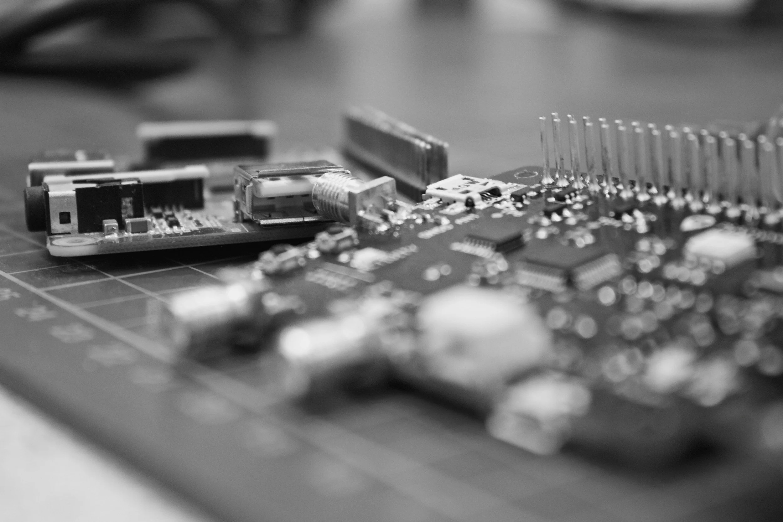Close-up of an electronic circuit board with various components, including a USB port, pins, and integrated circuits, on a work surface.