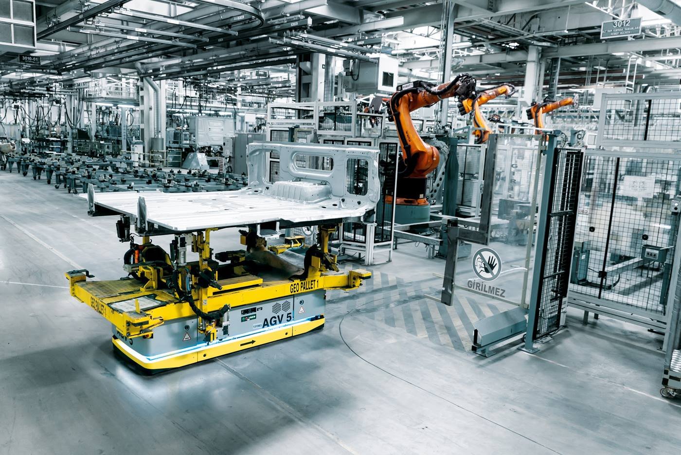 Automated industrial factory with robotic arms assembling a metal structure on a yellow moving platform.