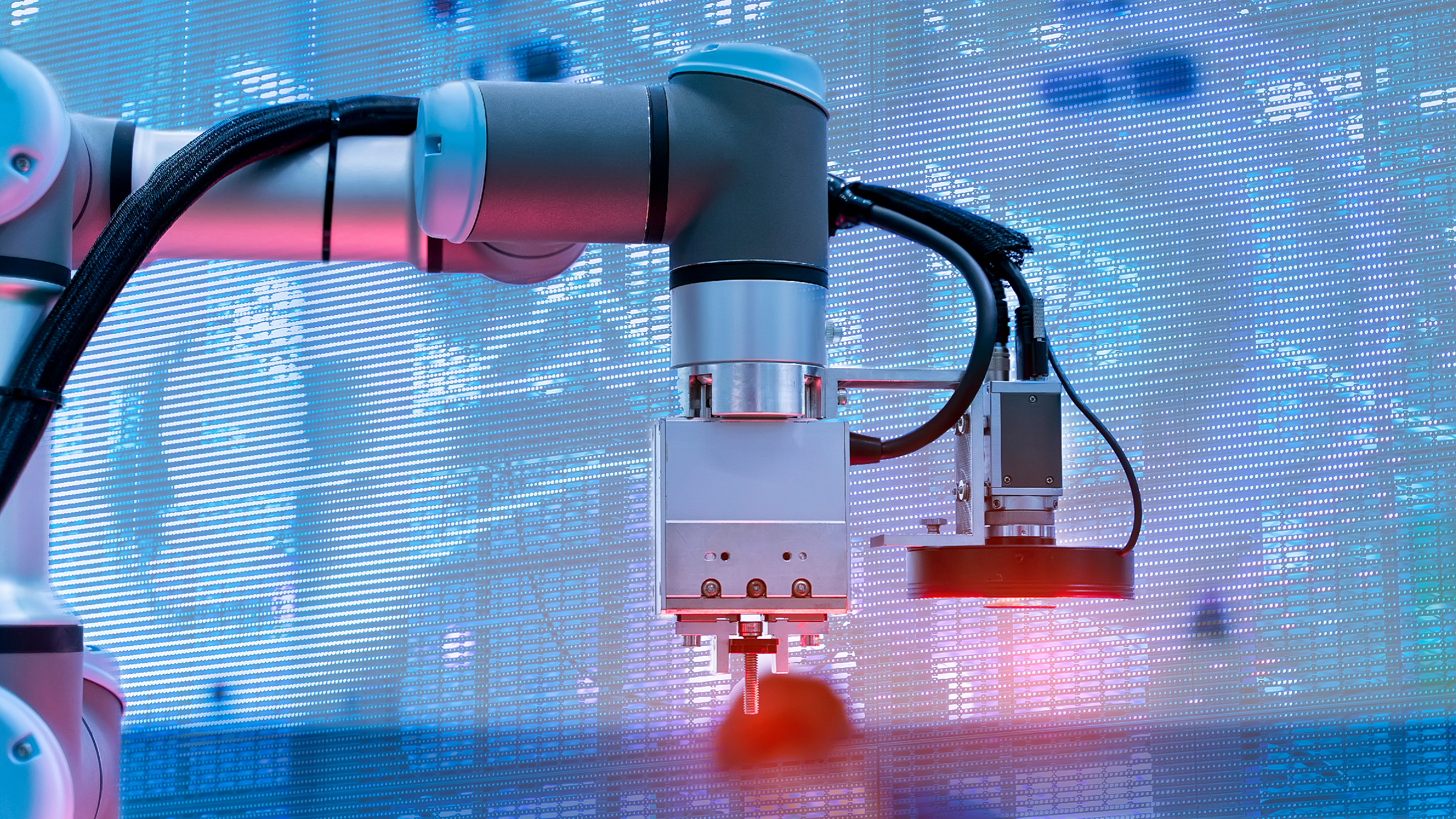 Close-up of an industrial robotic arm with a metallic and black finish, working on a manufacturing process against a bright digital blue background with a world map design.